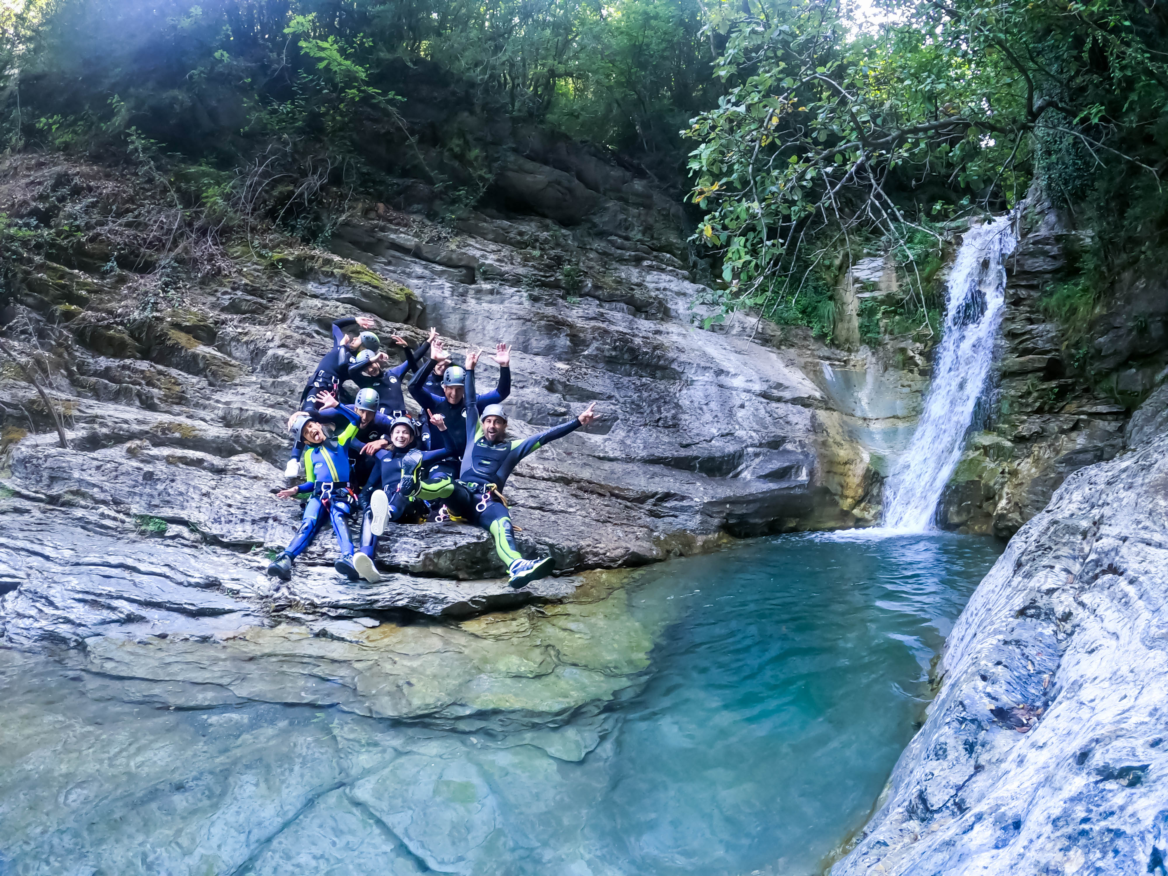 Barranquismo en el Pallars Jussà: grupo de participantes posando junto a una cascada y una poza de aguas cristalinas al finalizar una ruta de barranquismo en el Prepirineo de Lleida.