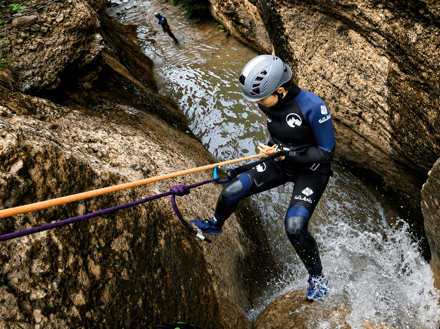 Barranquismo en el Pallars Jussà: participante realizando un rápel por una cascada en un barranco de roca con el guía esperando al fondo durante una ruta de barranquismo en el Prepirineo de Lleida.
