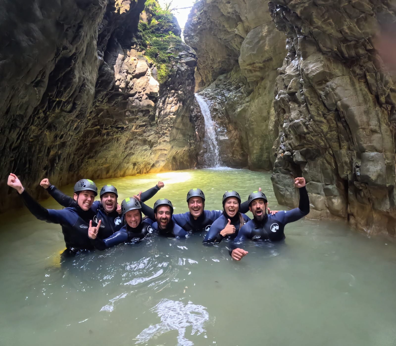 Grupo de participantes de barranquismo celebrando juntos en una poza natural bajo una cascada en el Barranco de Barbaruens
