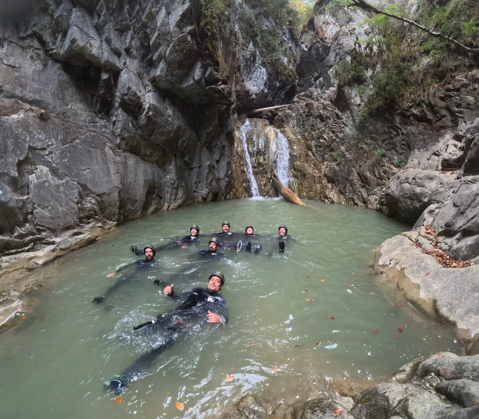 Grupo de participantes de barranquismo flotando y nadando en una poza natural bajo una pequeña cascada en el Barranco de Barbaruens