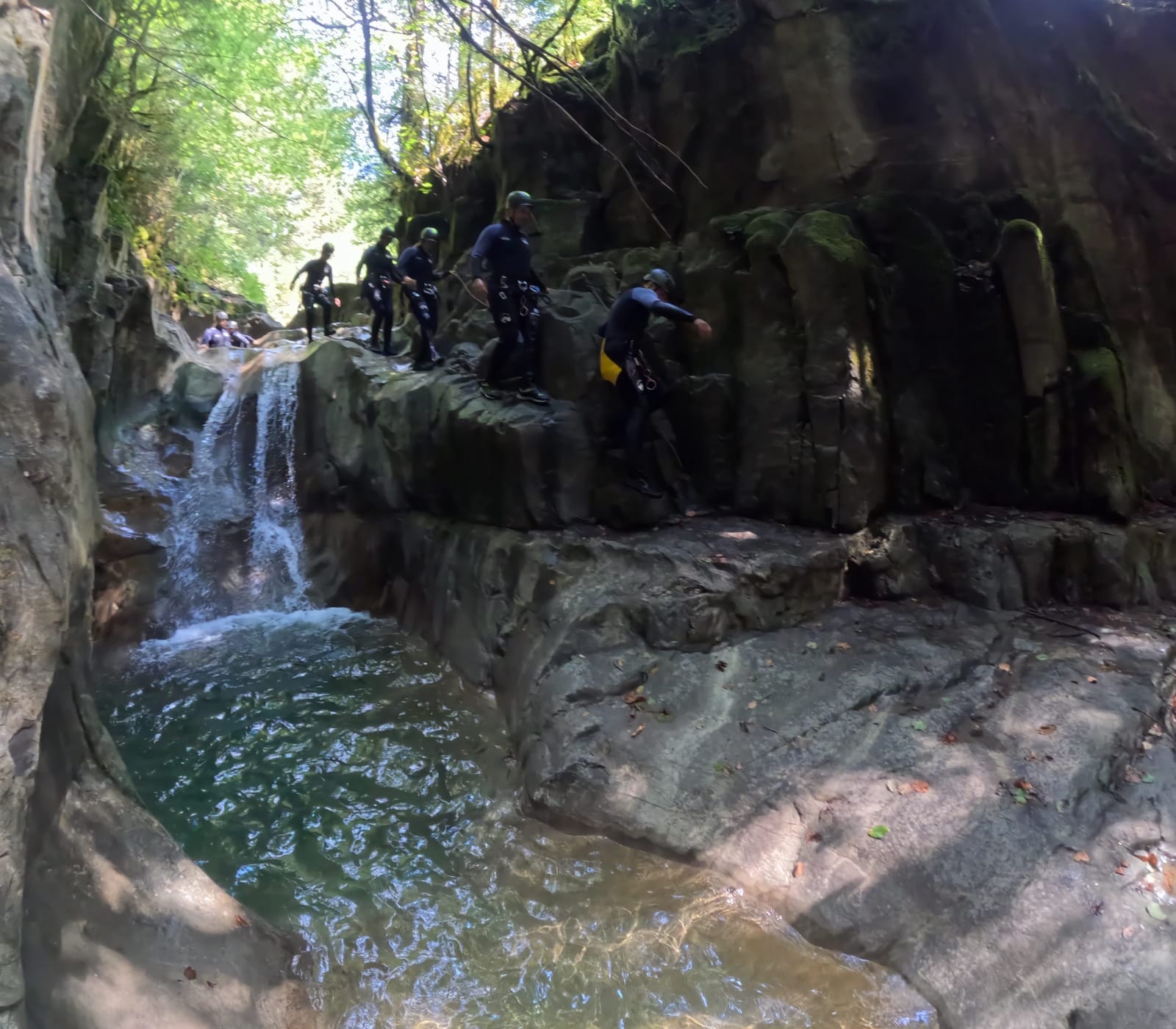 Grupo de barranquismo avanzando por las repisas rocosas junto a una pequeña cascada y una poza natural en el Barranco de Barbaruens