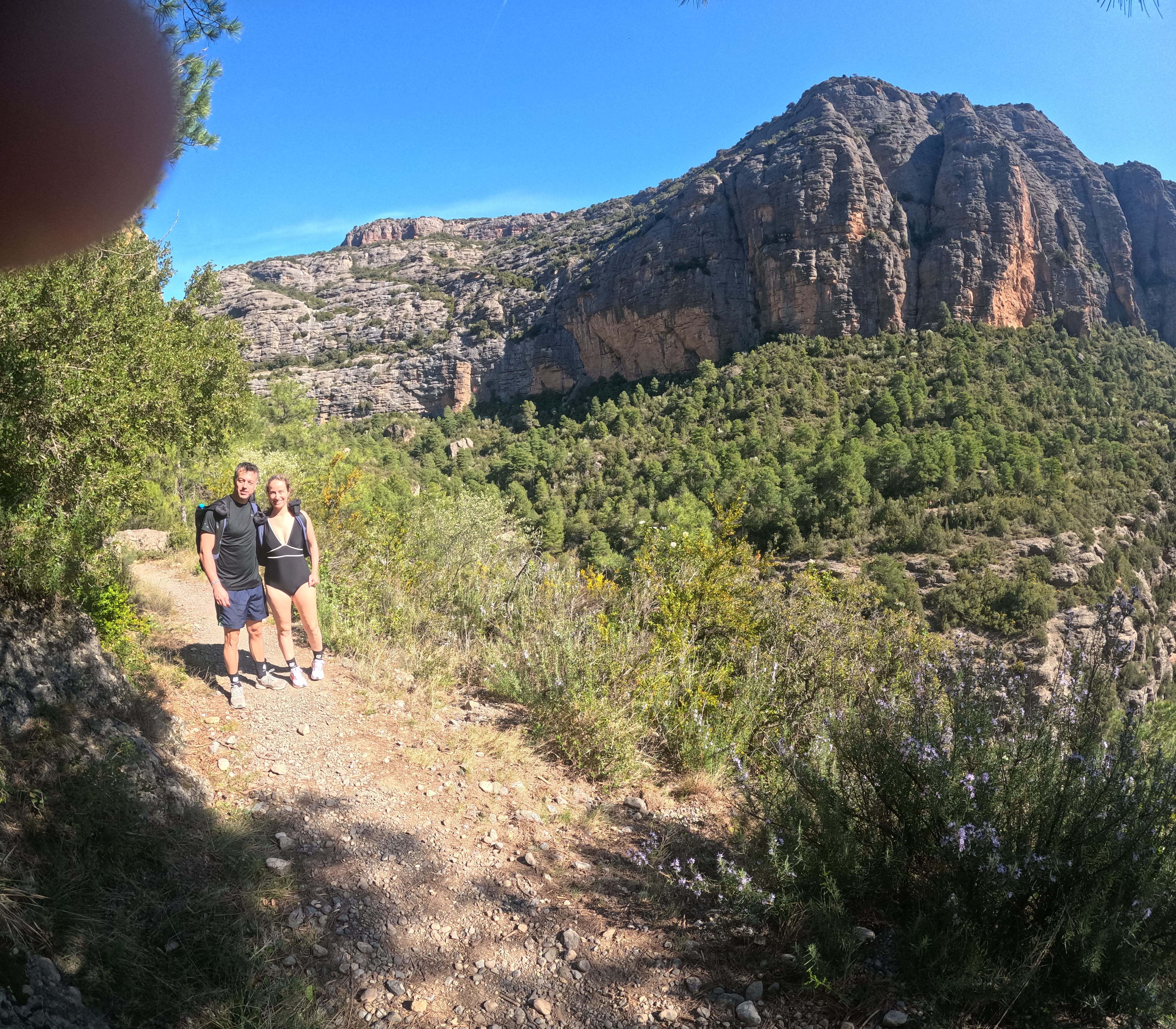 Two participants on the approach trail to Barranco Sant Pere with impressive rocky cliffs and mountain scenery in the background
