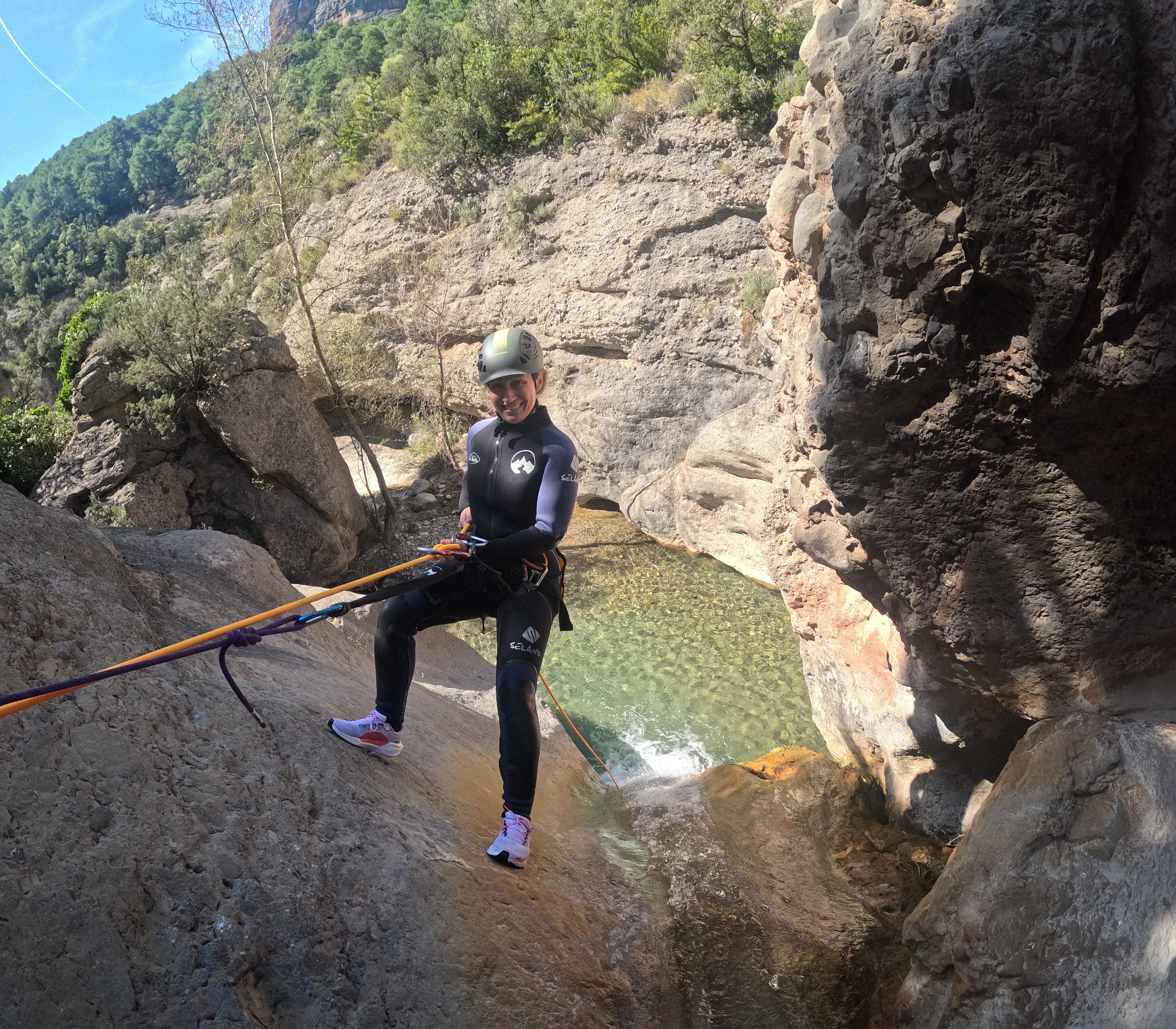Participant rappelling down a smooth rocky slope above a clear natural pool in Barranco Sant Pere