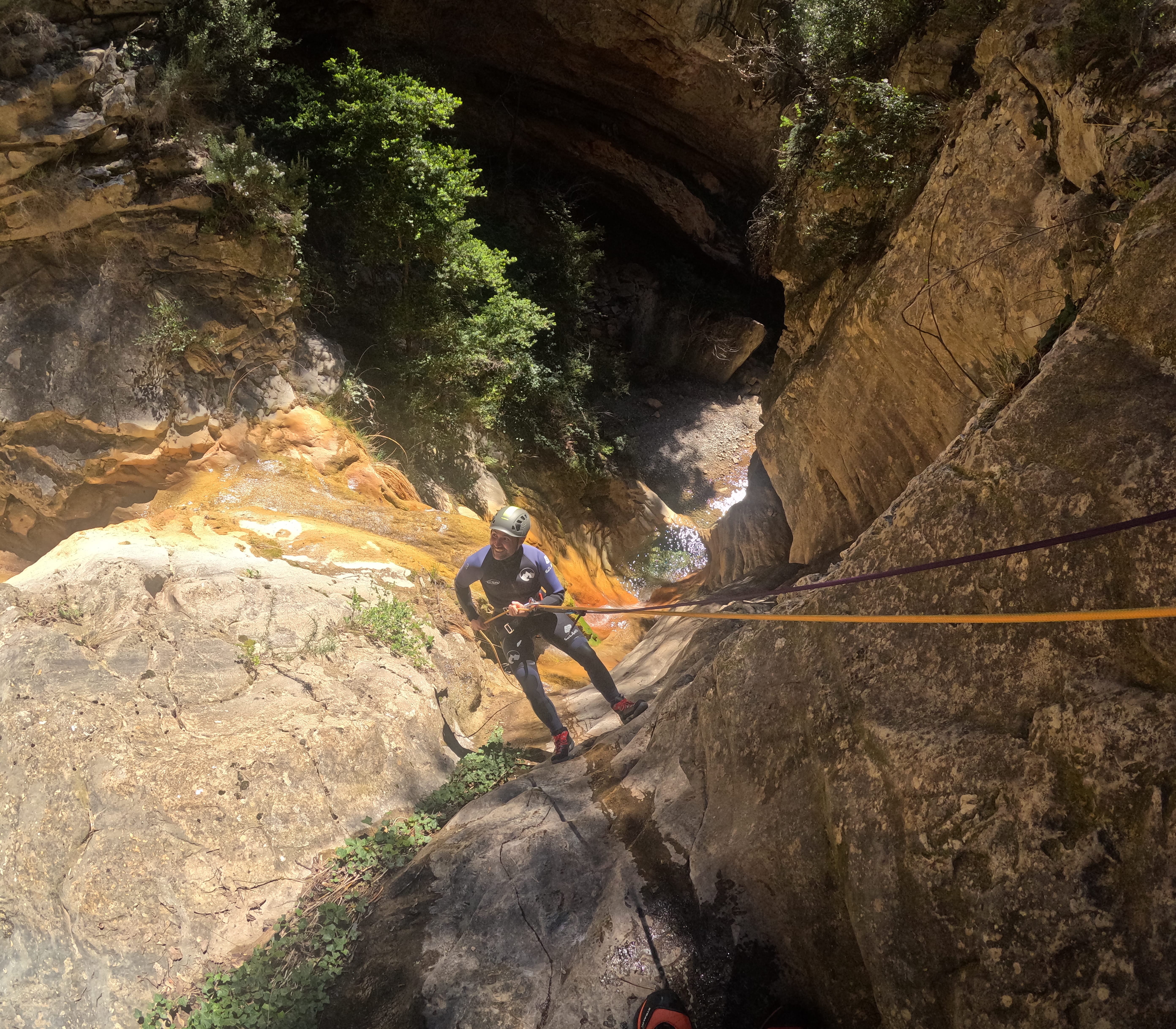 Participant rappelling down a steep rocky wall in Barranco de Gurp with the narrow canyon visible below