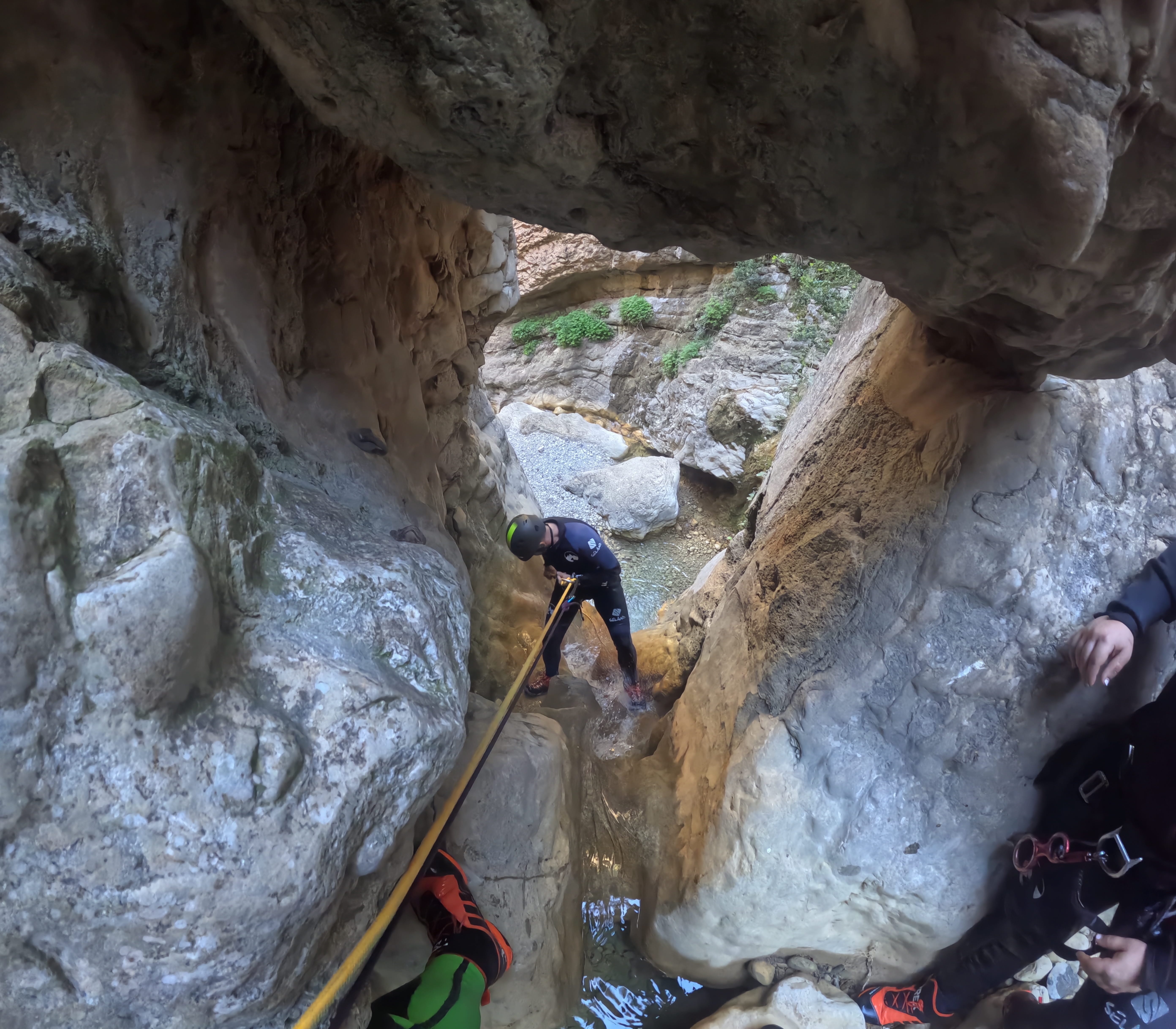 Participant descending with a rope through a narrow rocky passage with shallow water in Barranco de Gurp