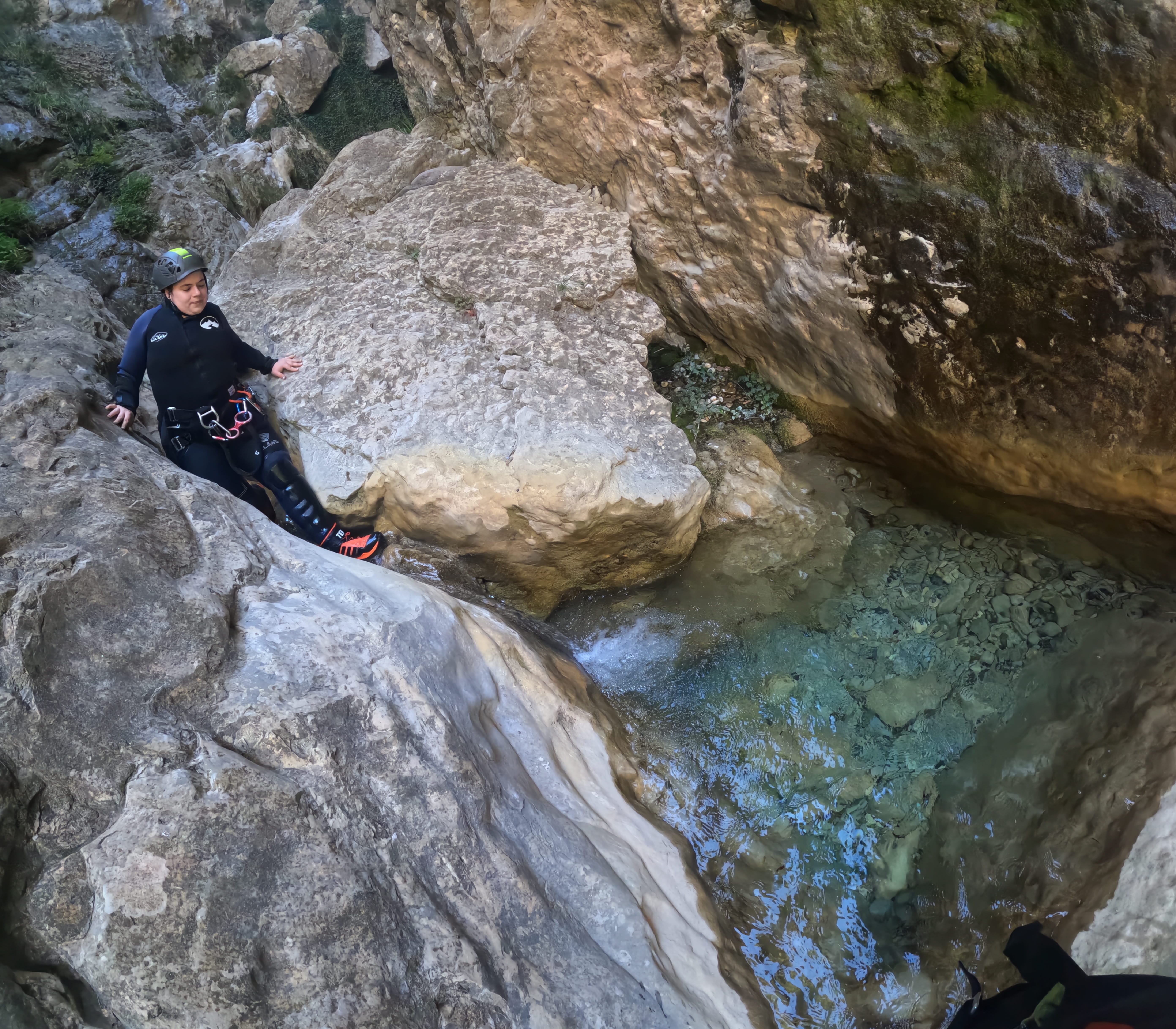 Participant carefully descending a smooth rocky chute beside a clear natural pool in Barranco de Gurp