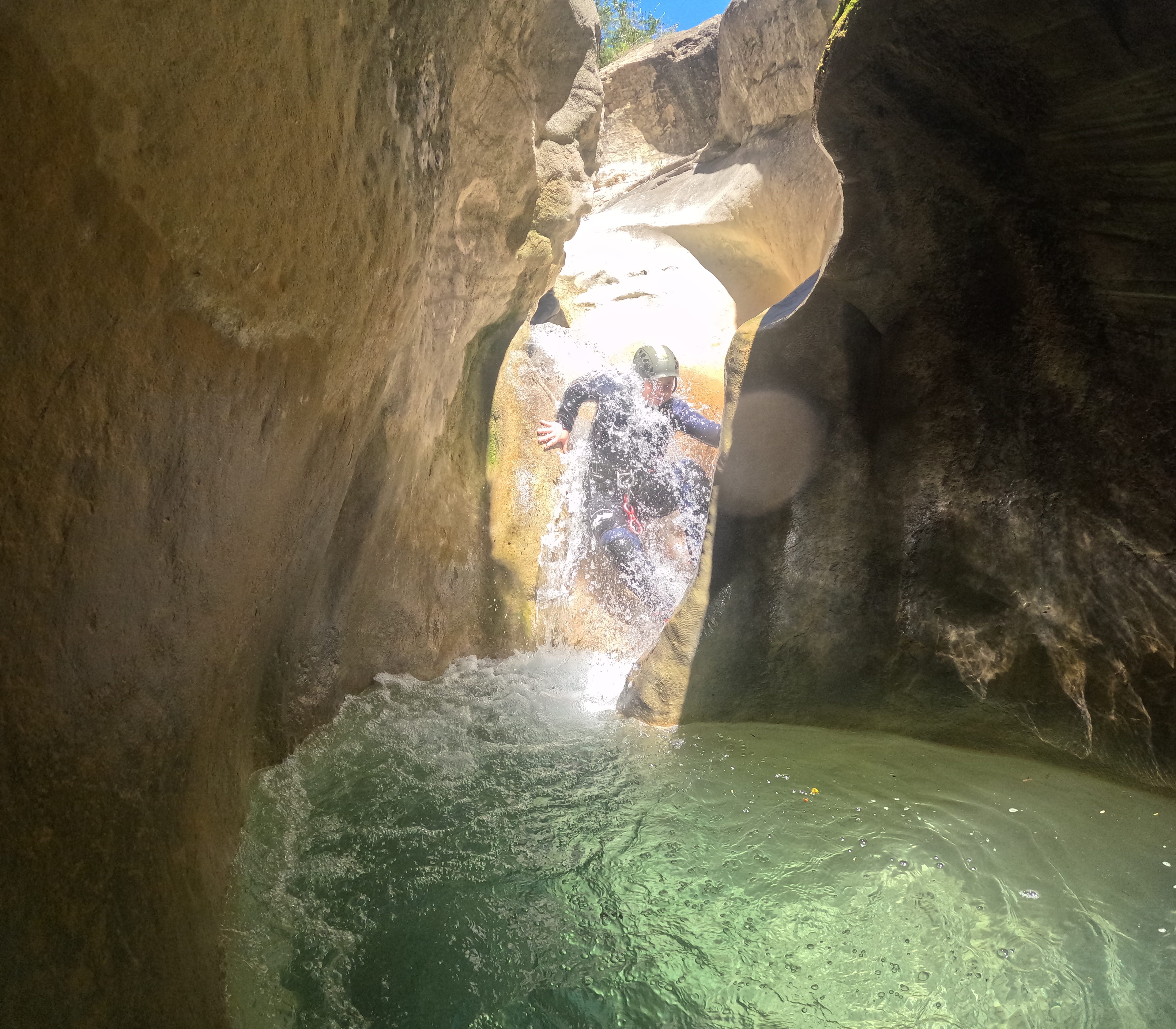 Participant sliding through a narrow waterfall into a turquoise natural pool in Barranco de Gurp