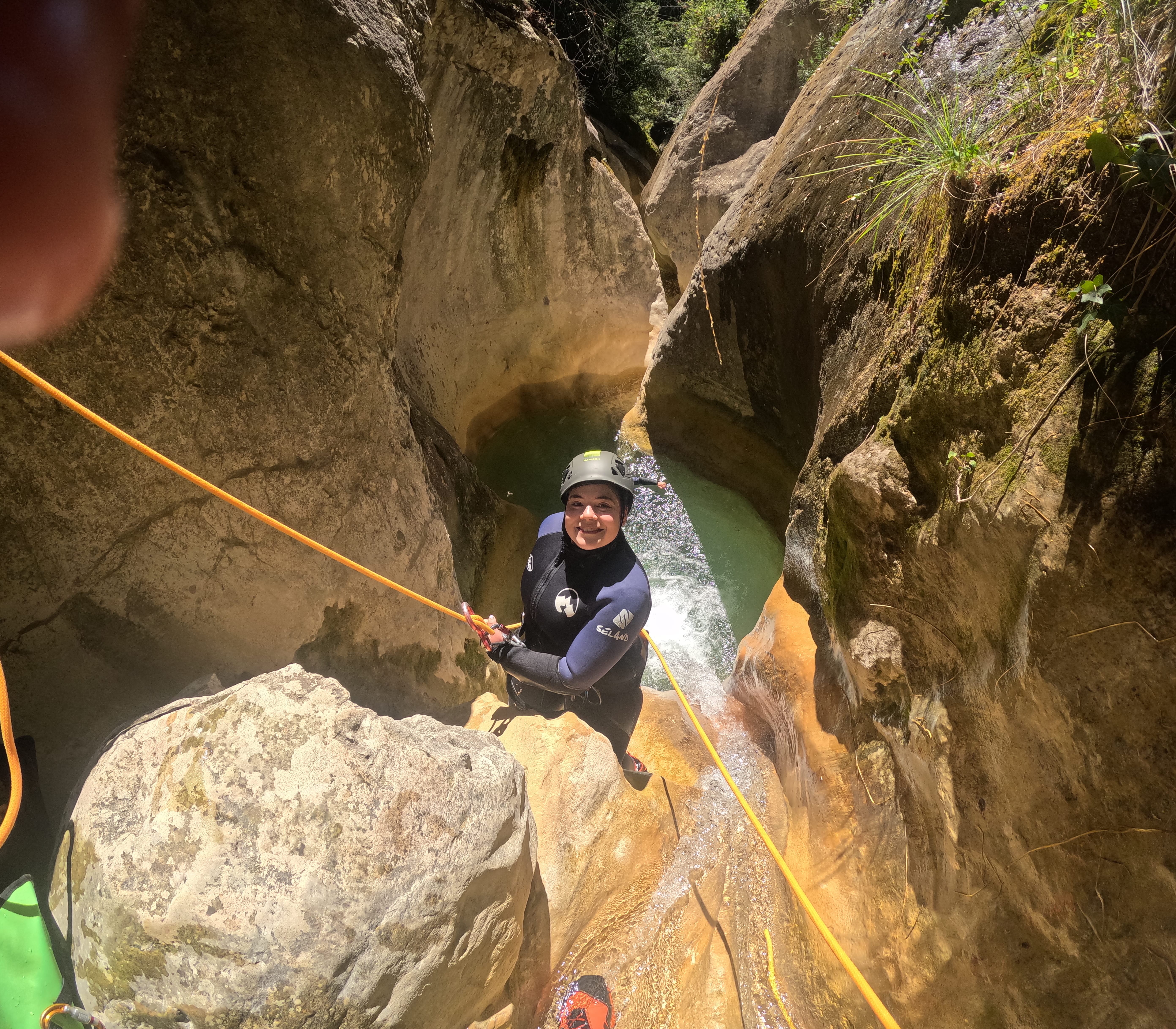 Participant rappelling through a narrow rocky section above a natural pool in Barranco de Gurp