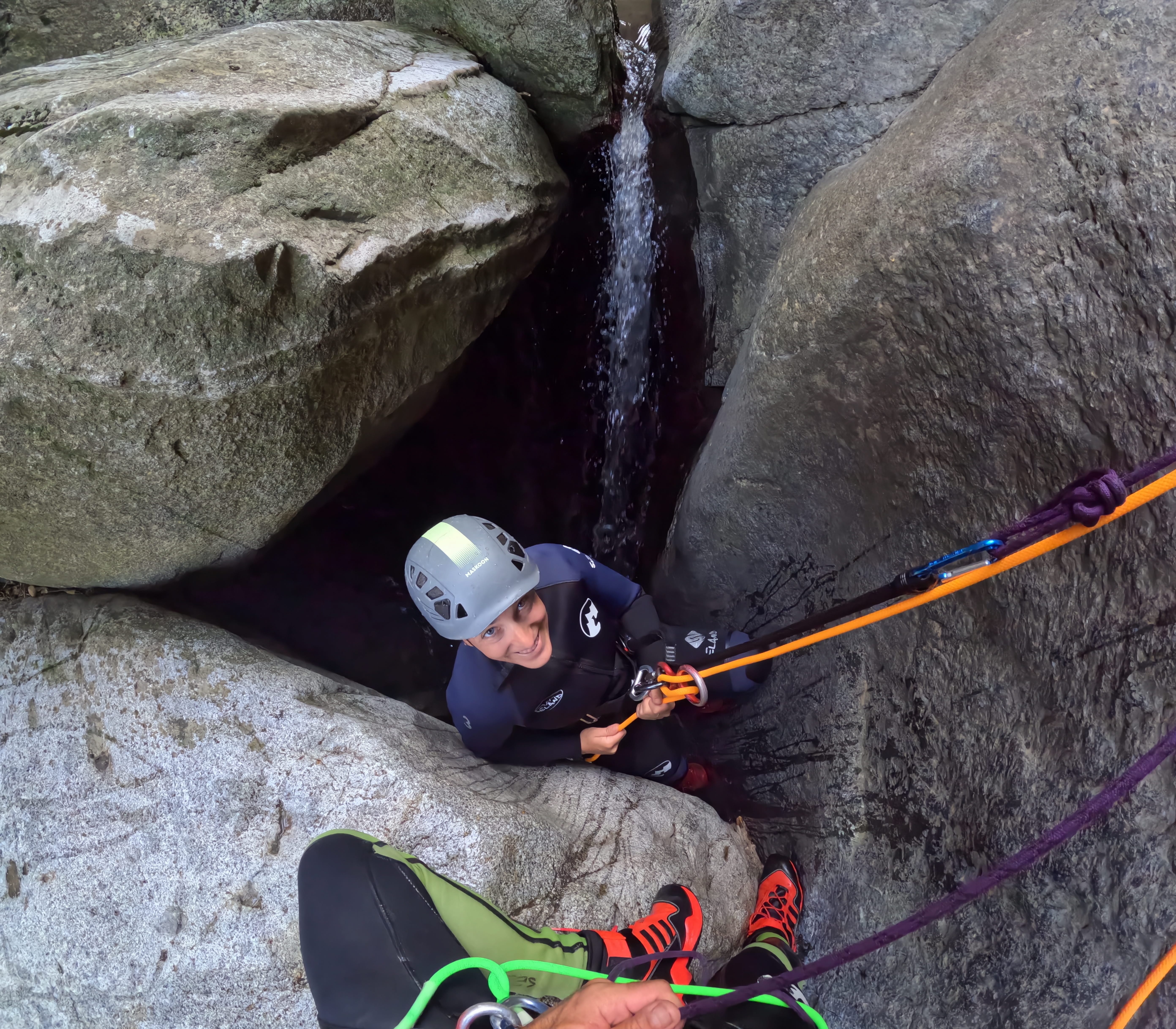 Participant rappelling between large rock walls next to a small waterfall in Barranco de Berrós
