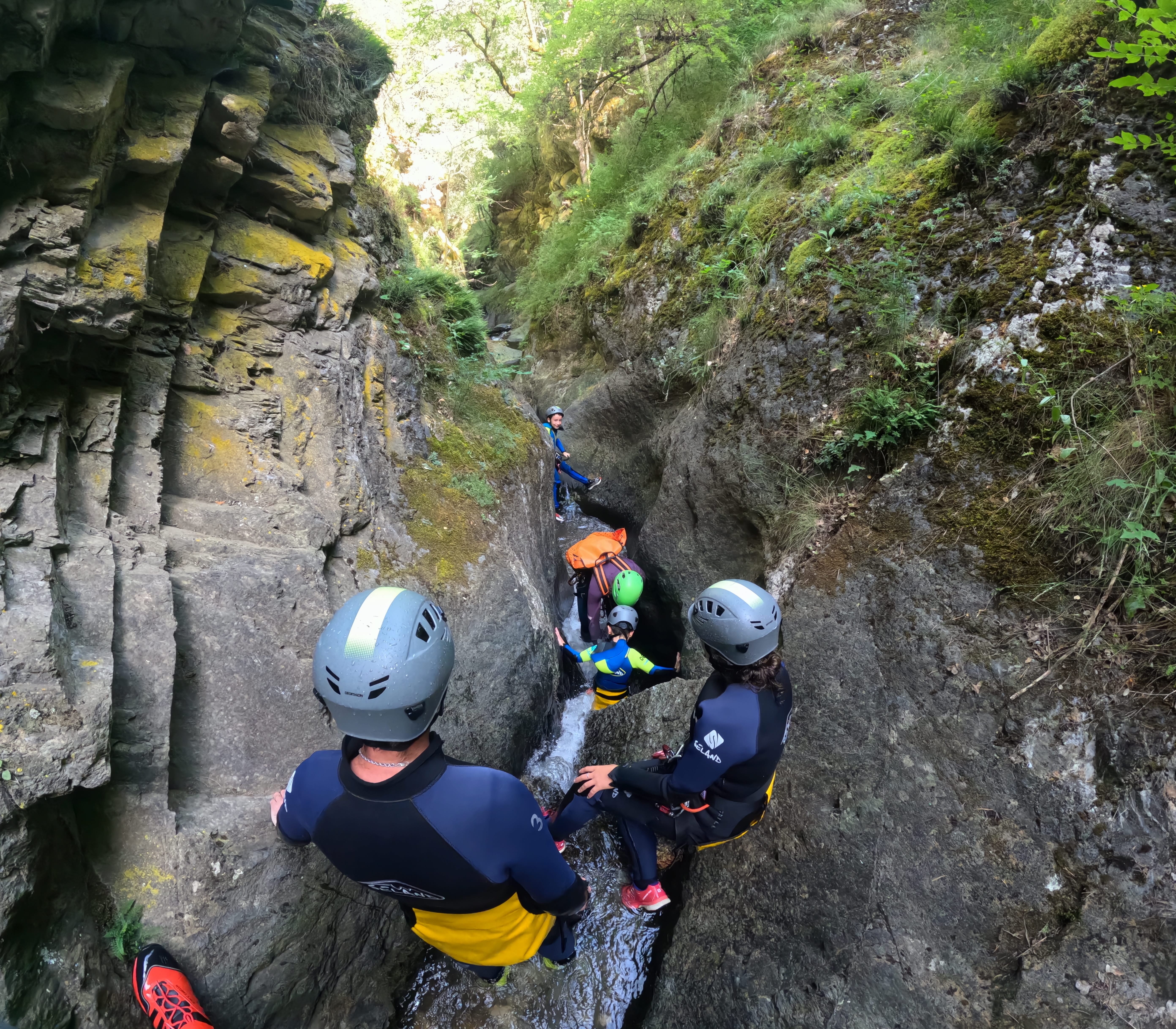 Group of participants descending through a narrow rocky gorge with flowing water during a canyoning route in Barranco de Berrós