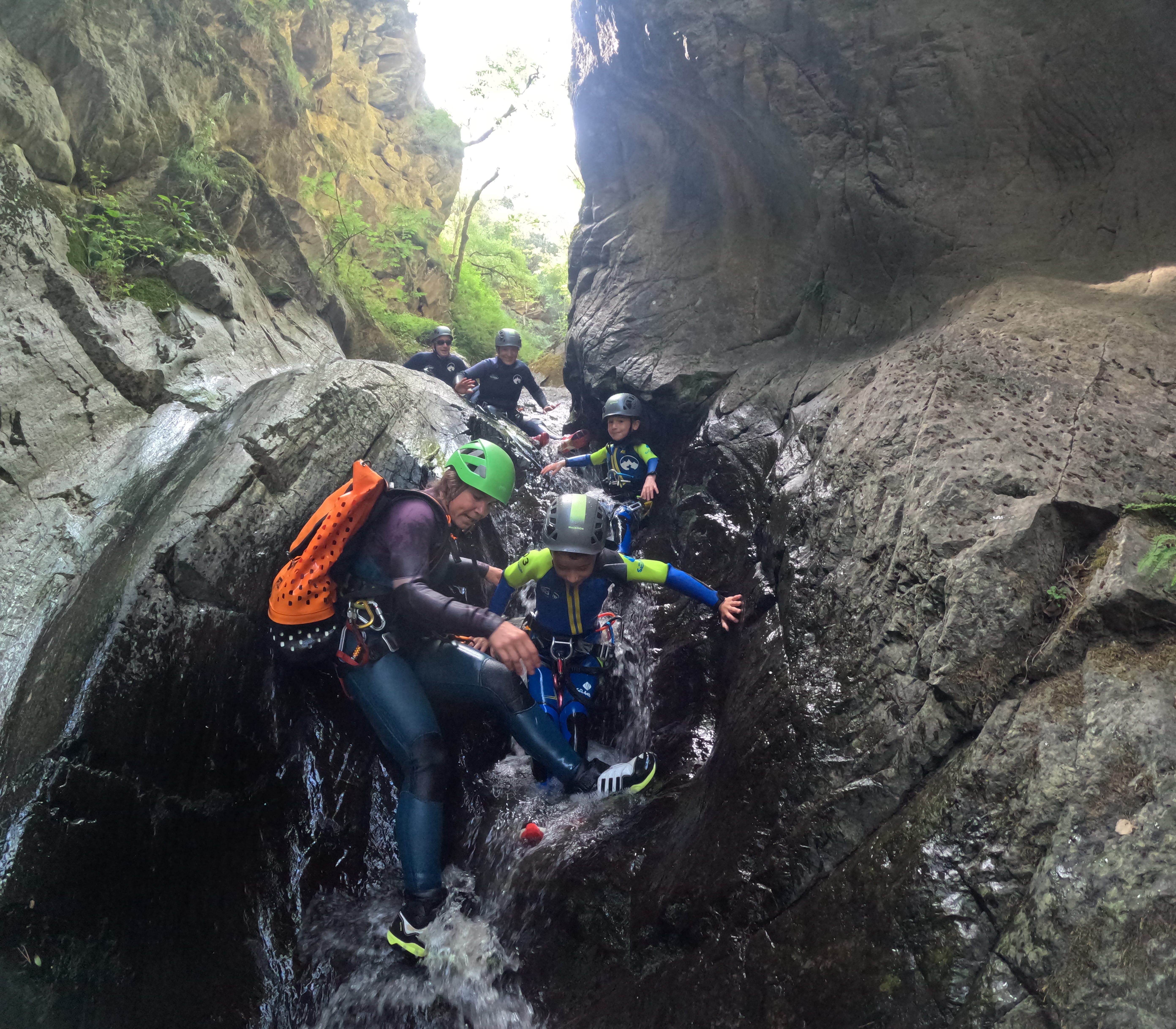 Guide assisting a child down a small waterfall during a family canyoning descent in Barranco de Berrós
