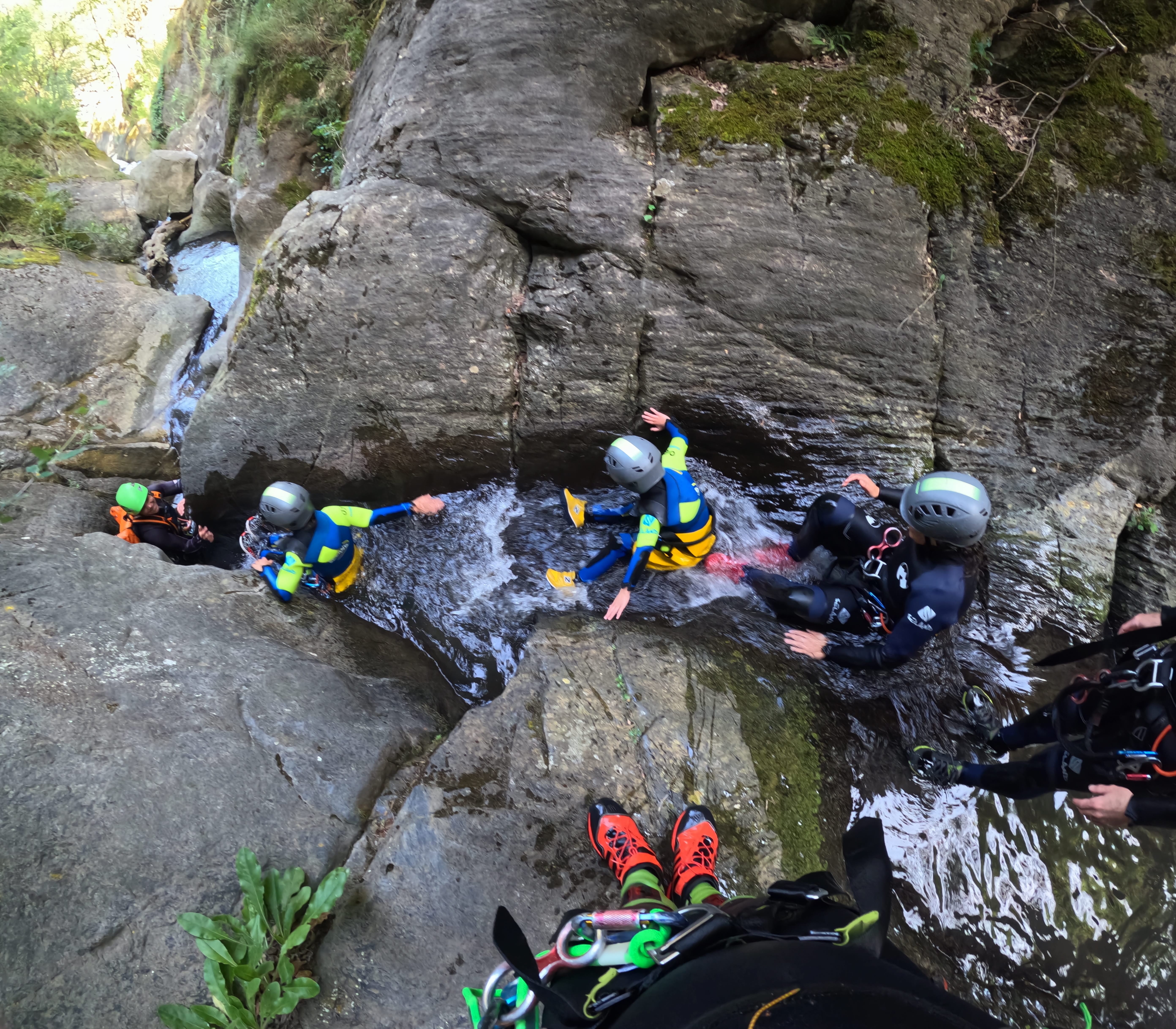 Adults and children moving through a narrow water-filled section of the canyon during a family canyoning descent in Barranco de Berrós