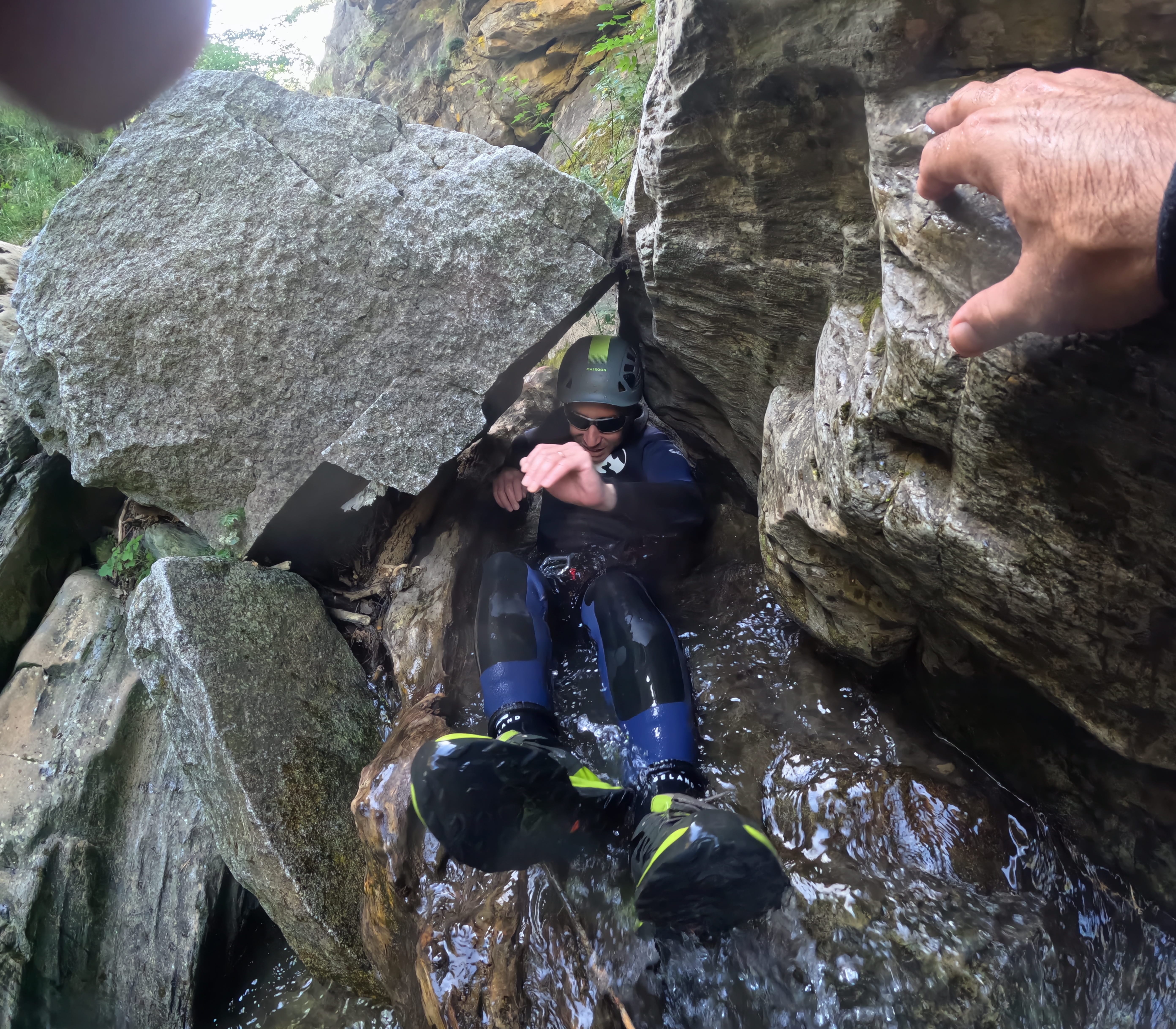 Participant sliding through a narrow rocky passage with flowing water during a canyoning descent in Barranco de Berrós