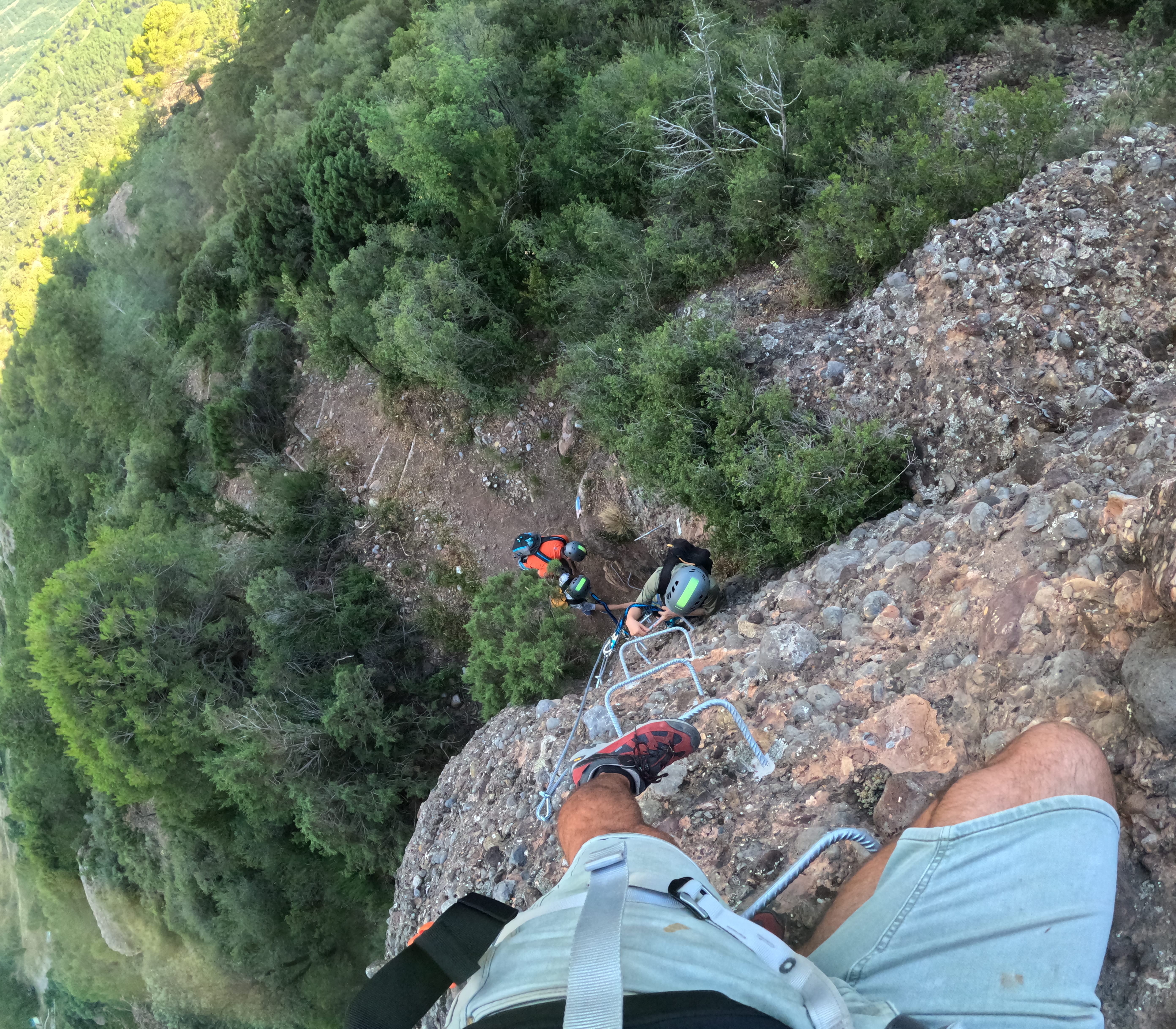 Climbers ascending a steep and exposed section of the Vía Ferrata Roca Foradada using metal rungs above the forest near La Pobla de Segur