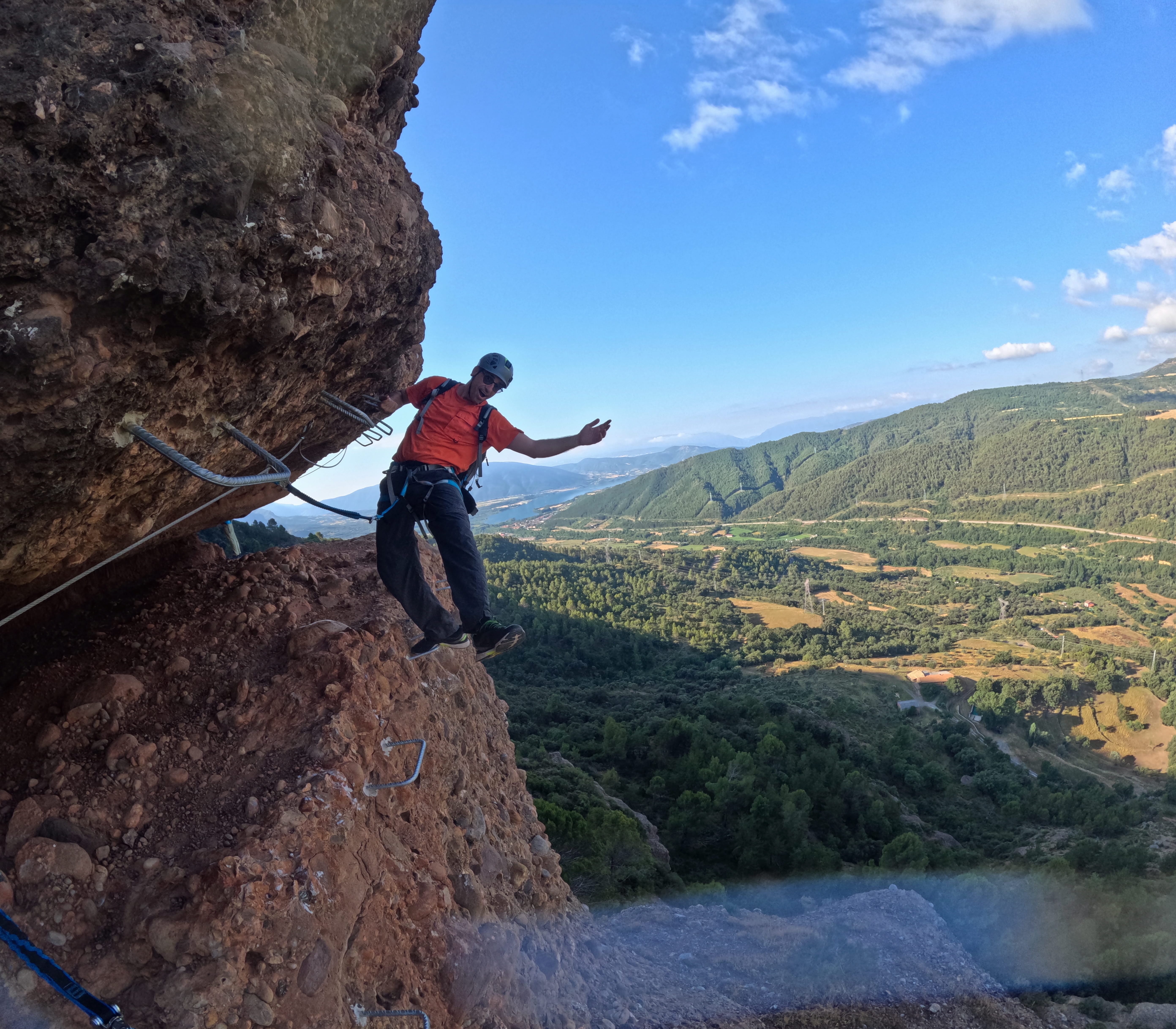 Climber traversing an exposed rocky section of the Vía Ferrata Roca Foradada with views over the valley and Sant Antoni reservoir near La Pobla de Segur