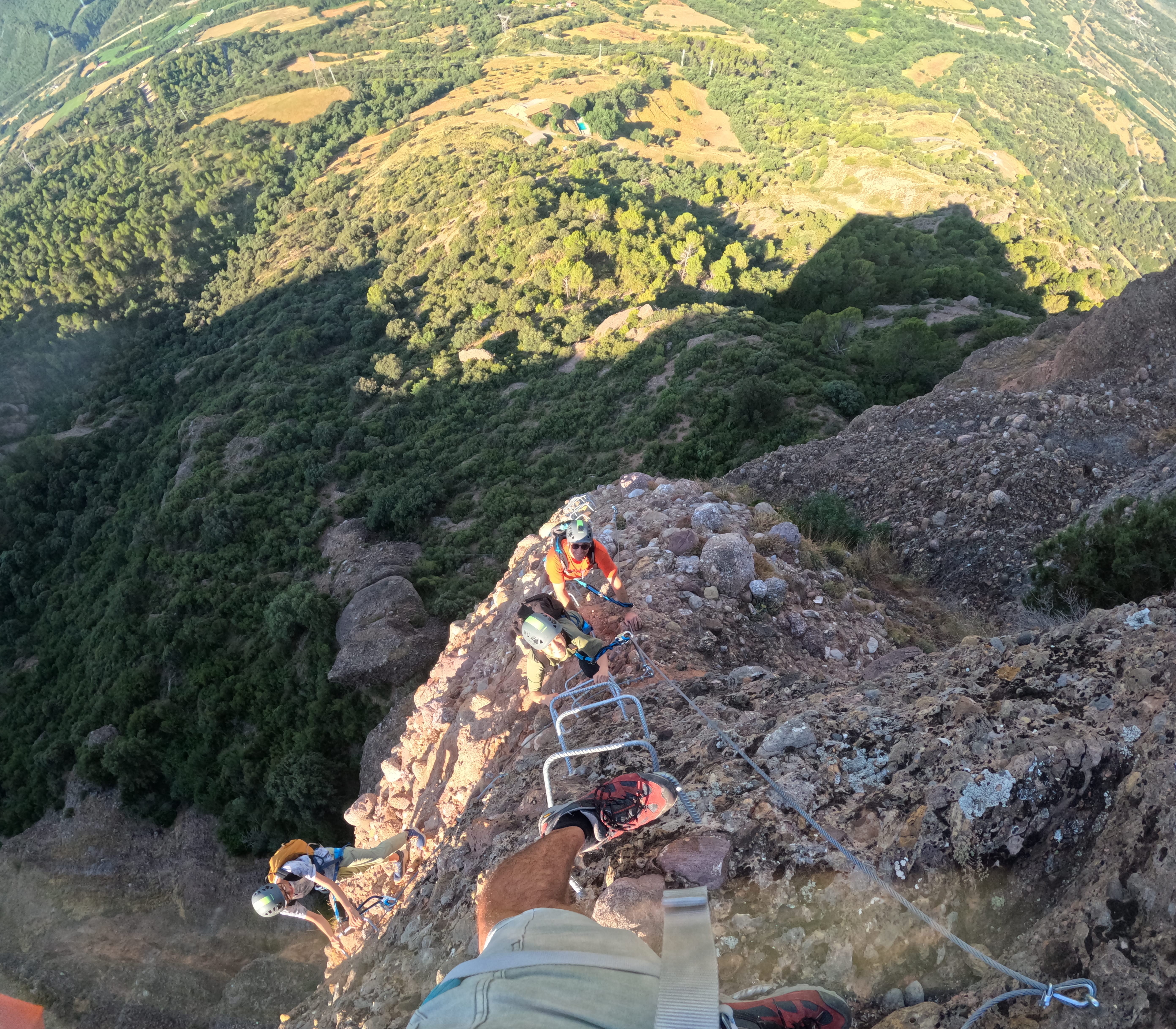 Climbers ascending a steep and exposed section of the Vía Ferrata Roca Foradada on metal rungs, with impressive views over the valley near La Pobla de Segur