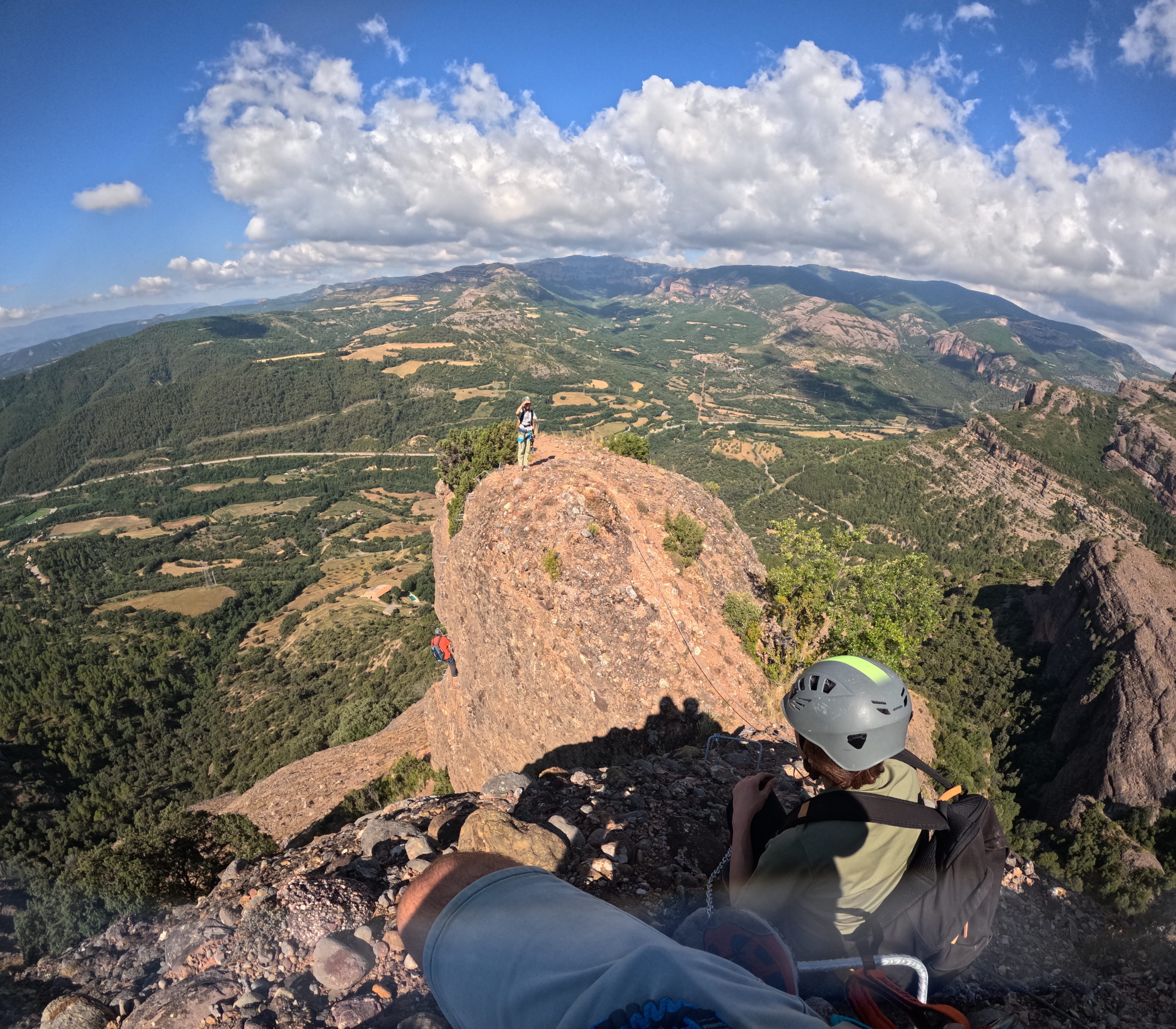 Climbers on the exposed ridge of the Vía Ferrata Roca Foradada, with spectacular panoramic views of the mountains and valley near La Pobla de Segur