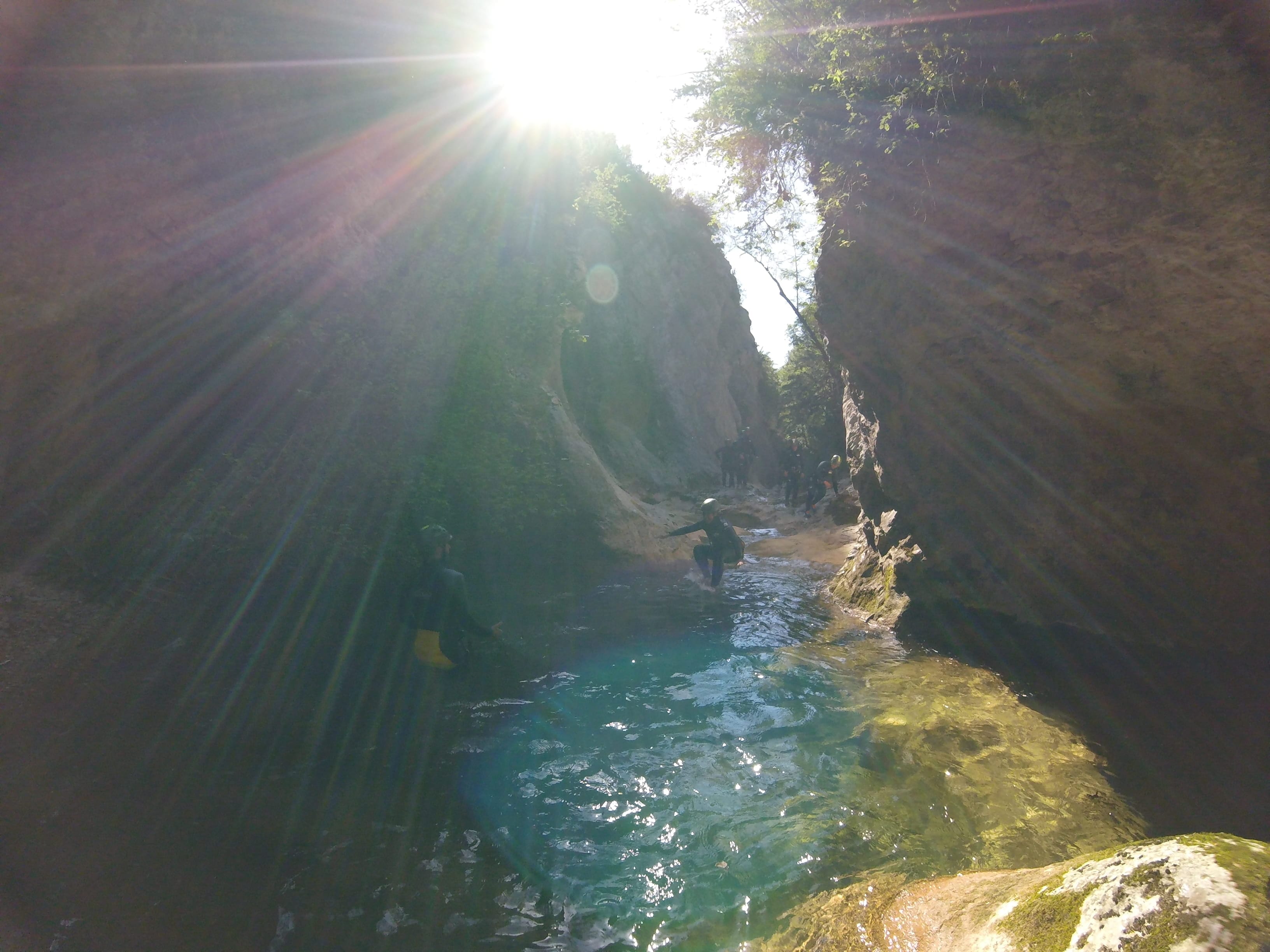 Canyoning group moving through a sunlit natural pool between steep rock walls in Barranc de Viu de Llevata