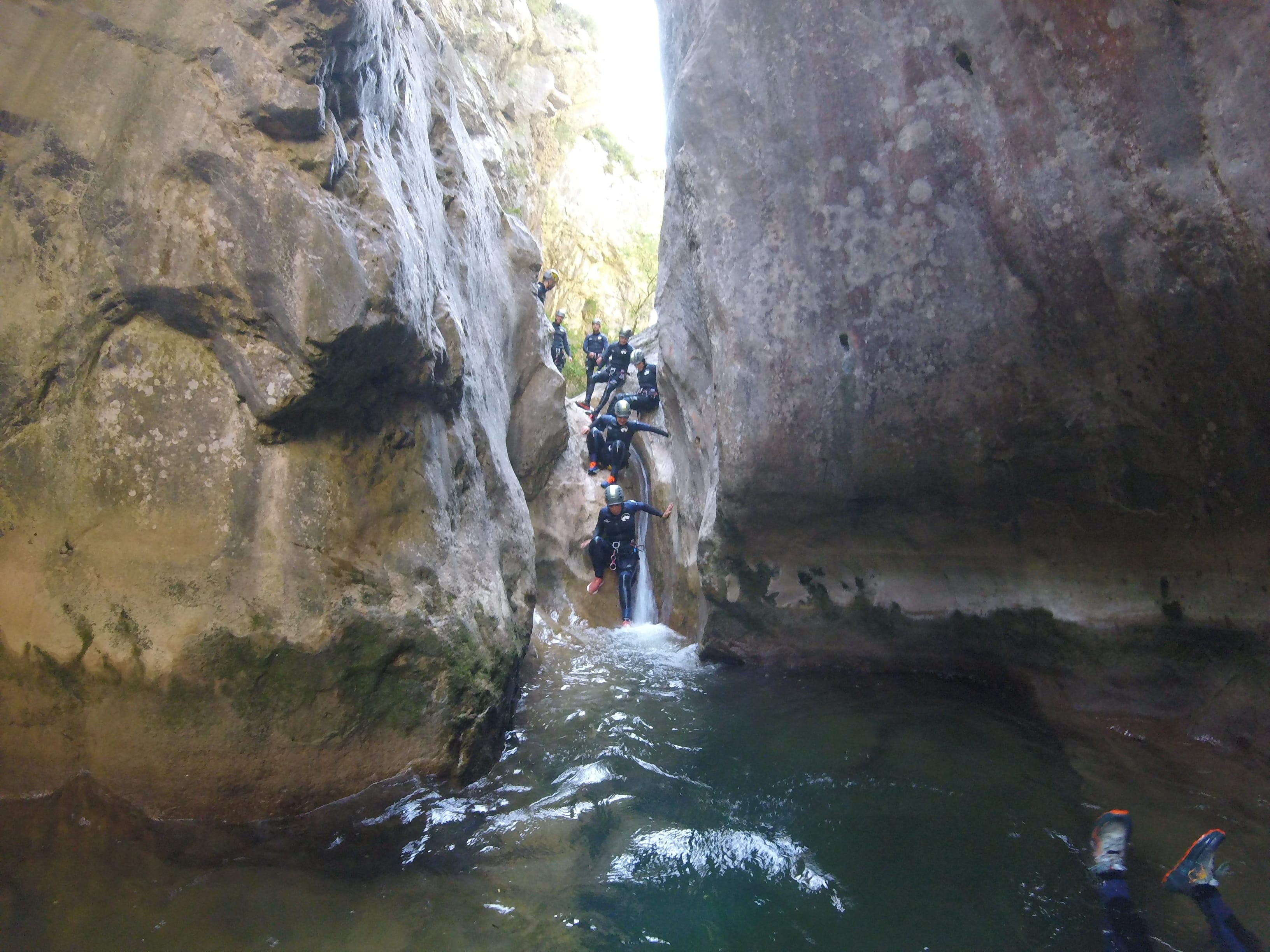 Canyoning group descending a small waterfall into a natural pool between narrow rock walls in Barranc de Viu de Llevata