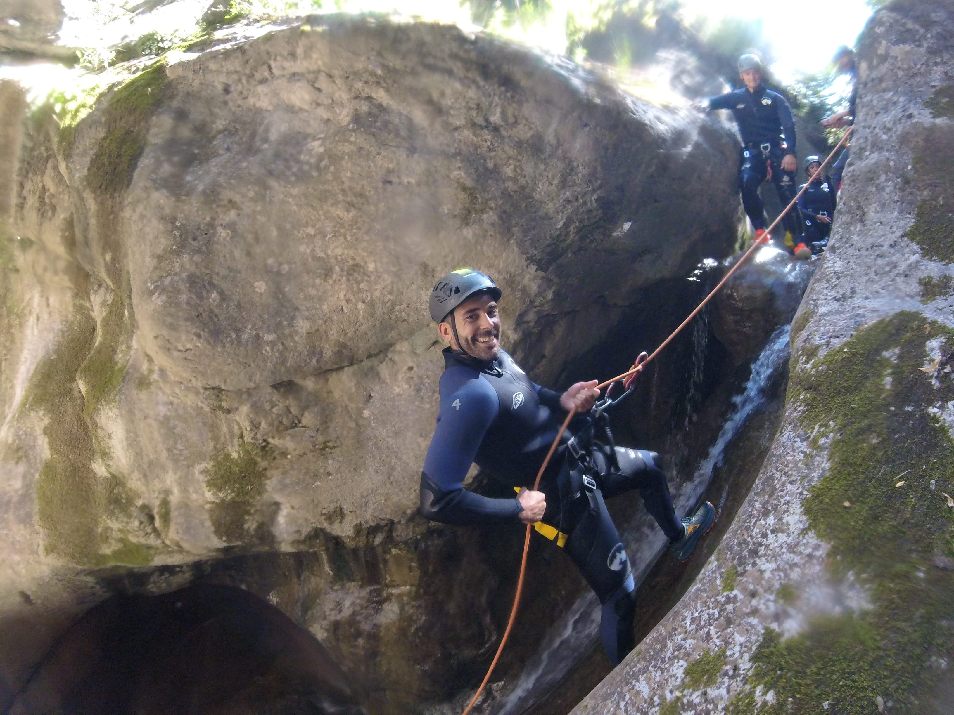 Canyoning participant rappelling beside a small waterfall between rock walls in Barranc de Viu de Llevata