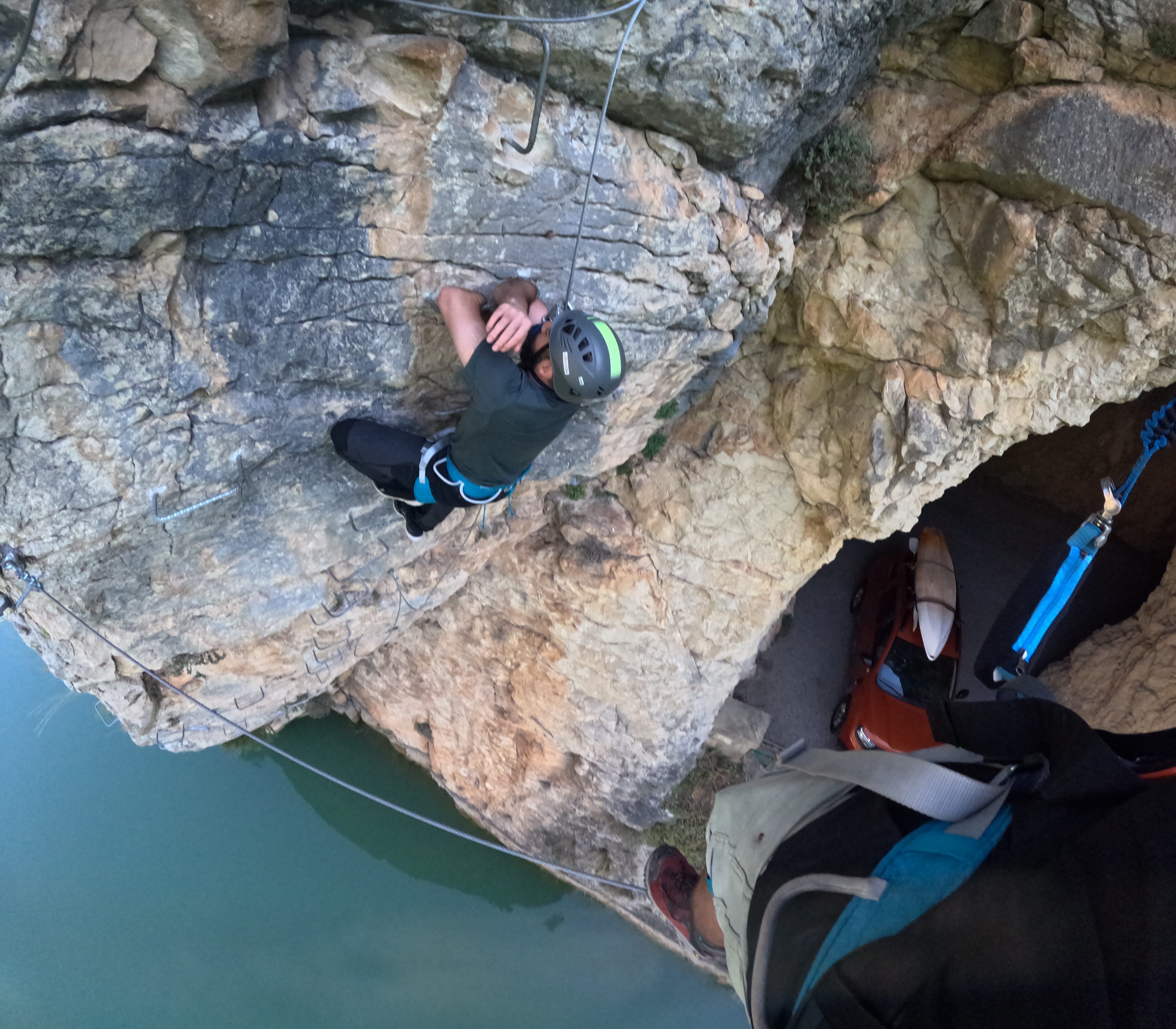 Participant climbing a demanding overhanging section of the vía ferrata Les Arcades above the reservoir, using metal rungs and secured to the safety cable