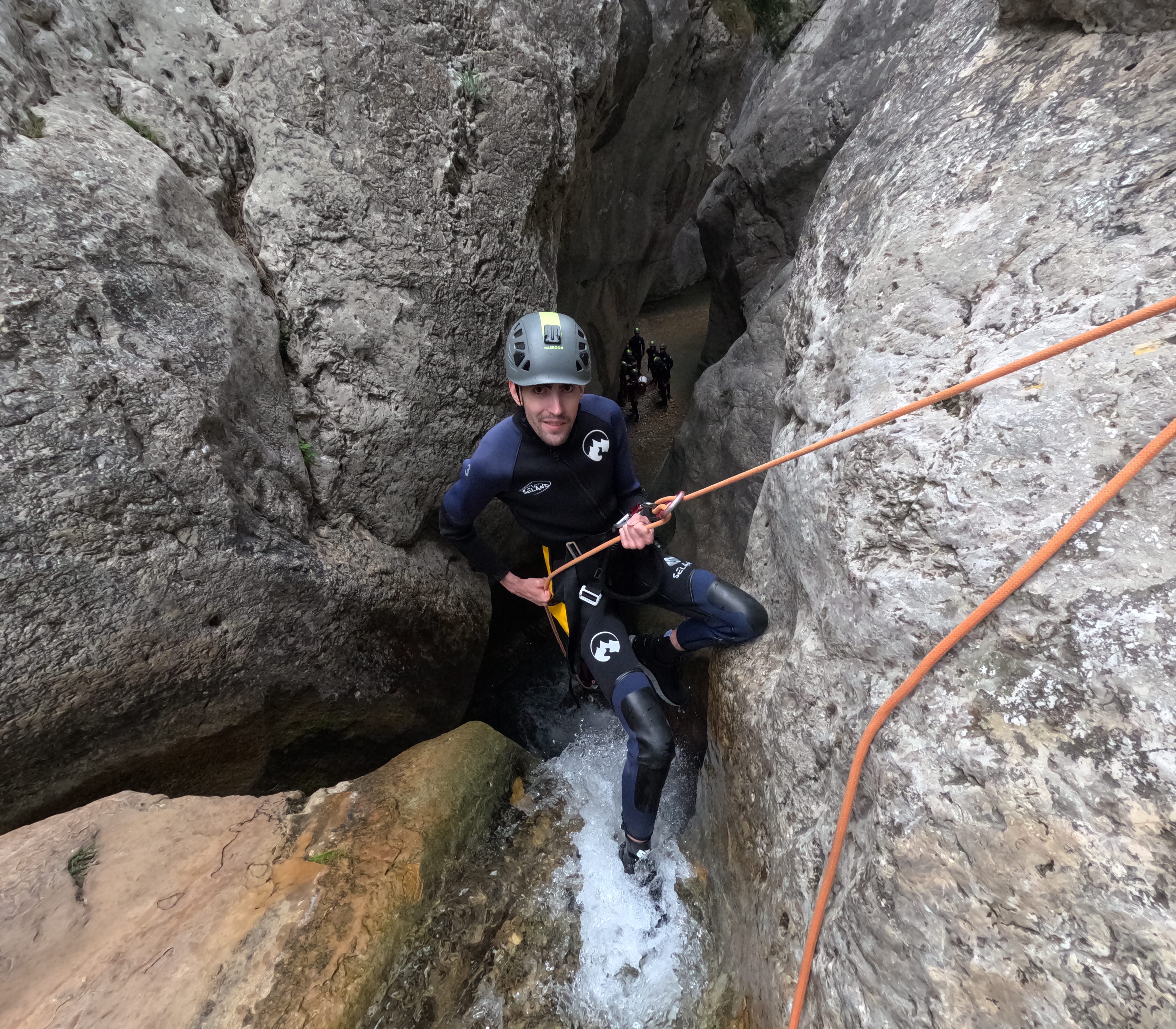 Canyoning participant descending on a rope through a narrow rocky passage with flowing water in Barranco de Bóixols