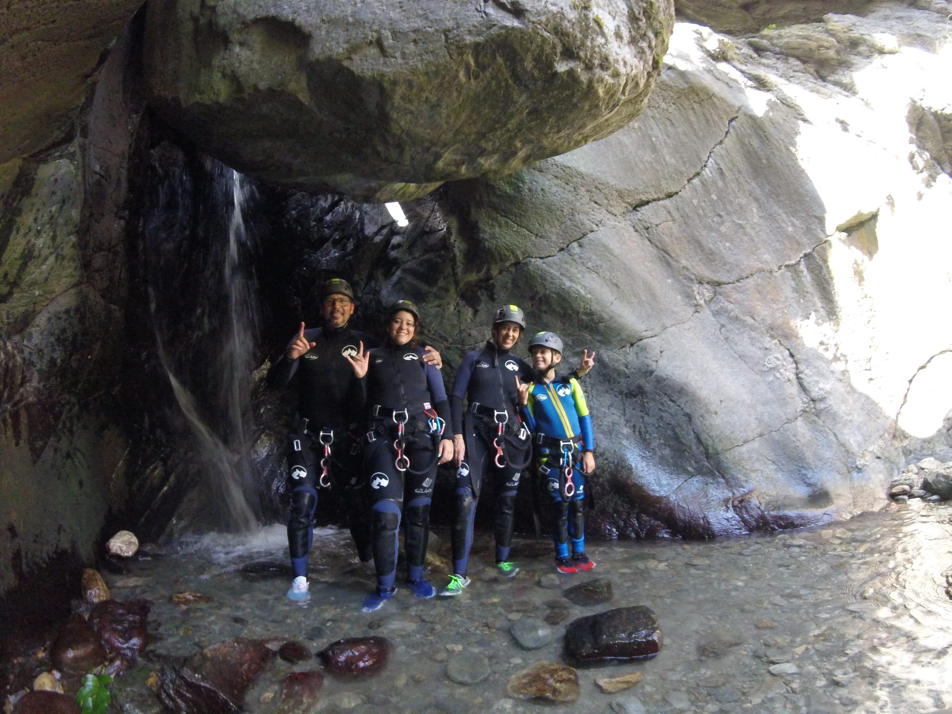 Canyoning group posing beneath a rock overhang beside a small waterfall in Barranco de Berrós