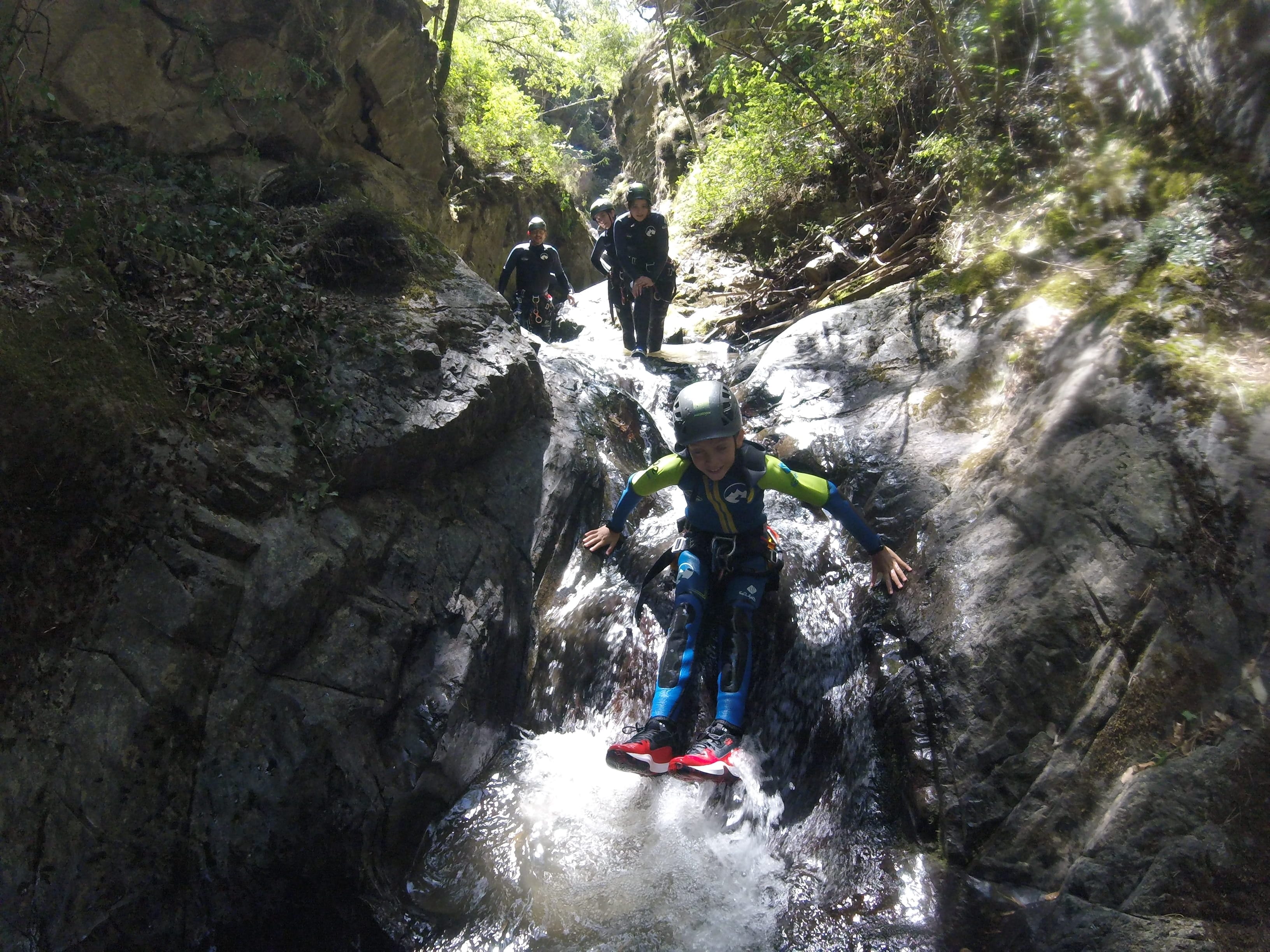 Young participant sliding down a small rocky waterfall during a canyoning descent in Barranco de Berrós