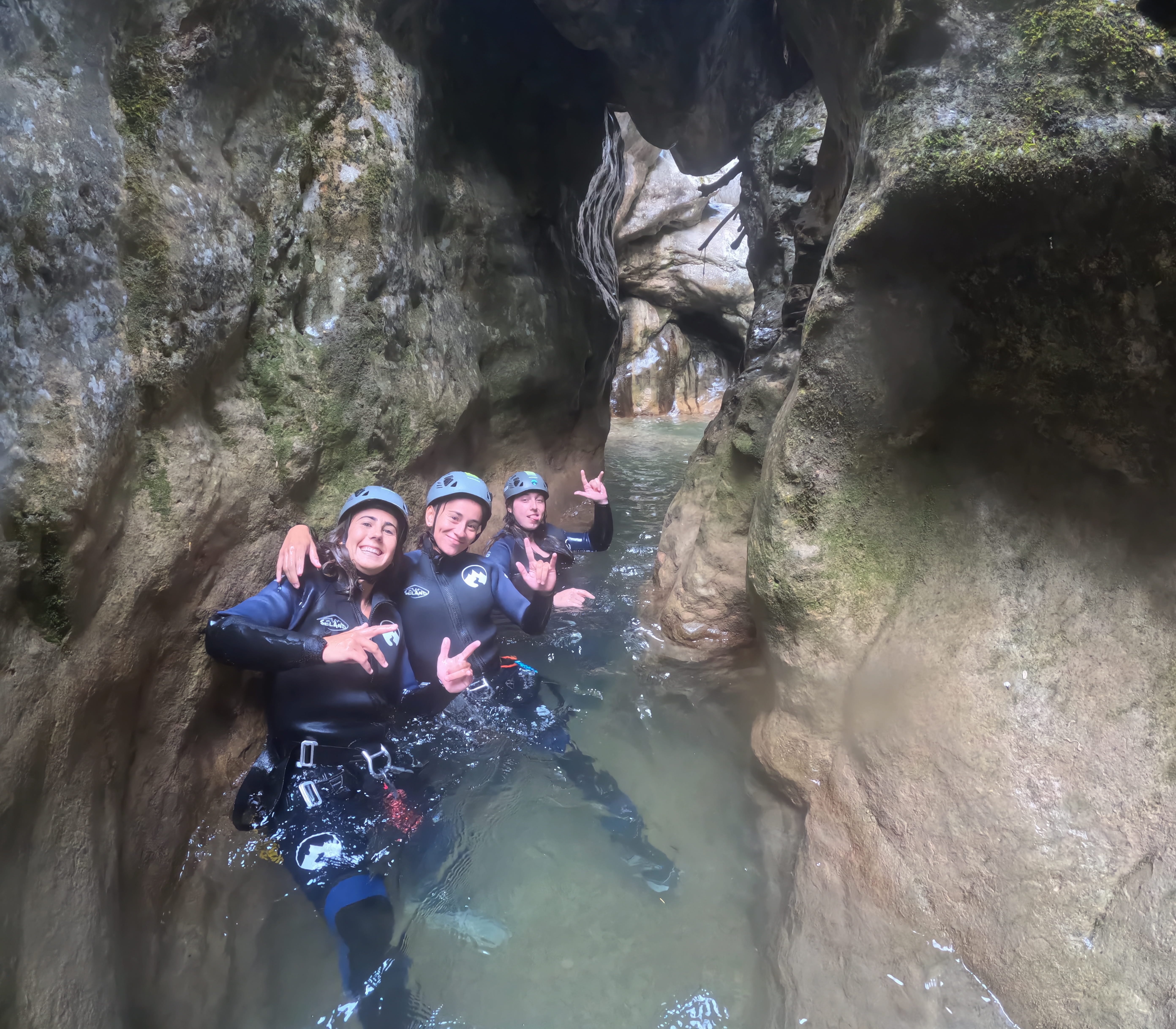 Three canyoning participants moving through a narrow water-filled gorge in Barranc de Viu de Llevata