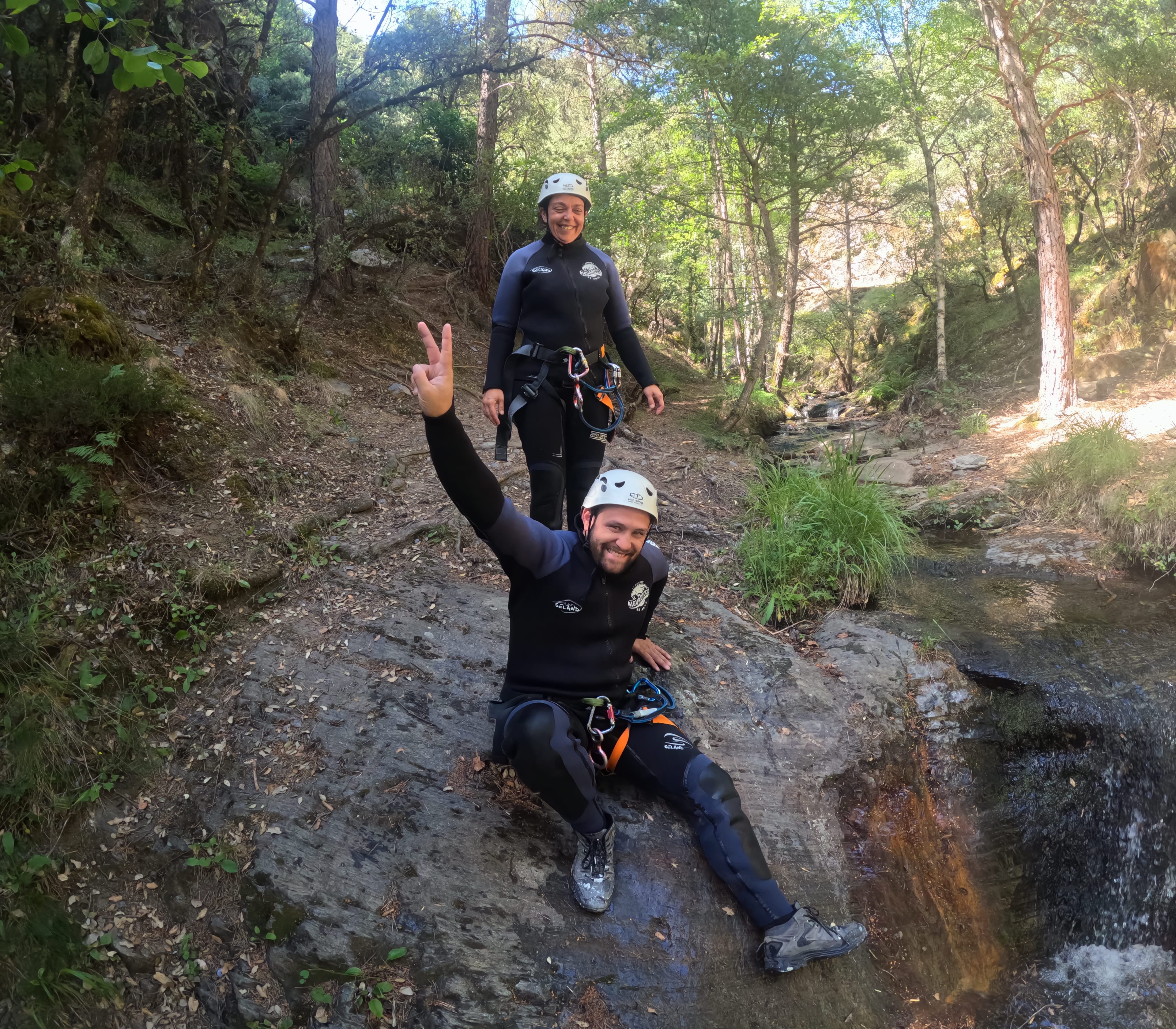 Two canyoning participants relaxing and smiling beside a forest stream in Barranco de Estaron