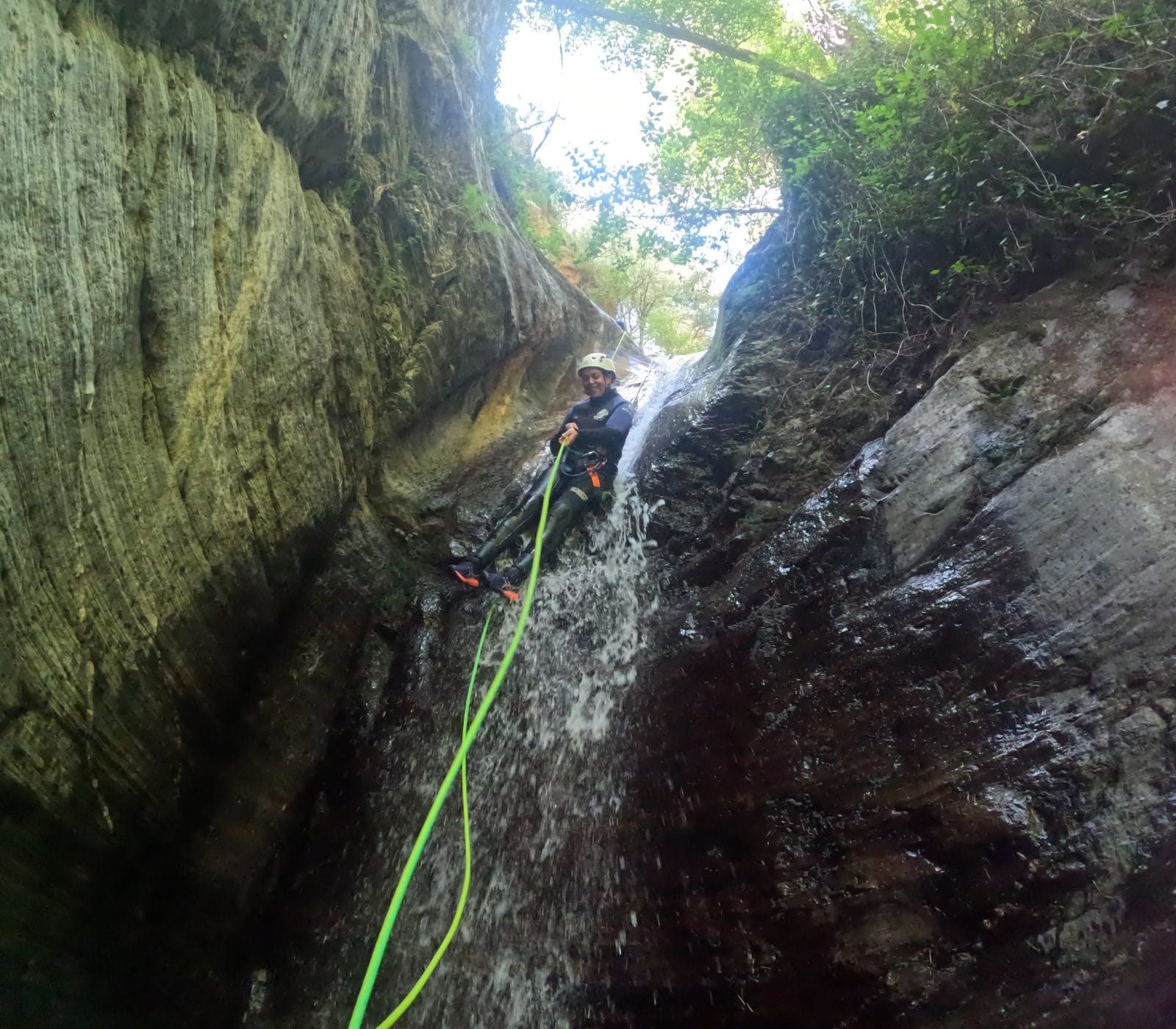 Canyoning participant rappelling down a waterfall with a rope in Barranco de Estaron