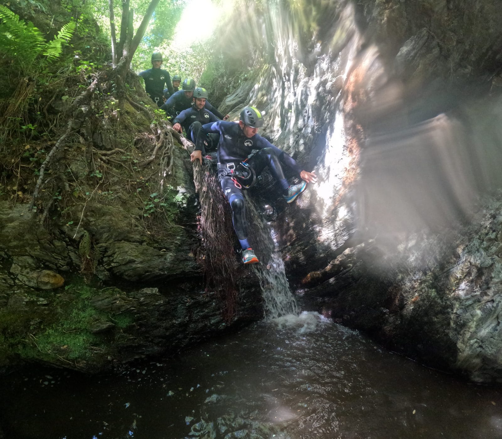 Canyoning participants descending a small waterfall into a natural pool in Barranco de Estaron
