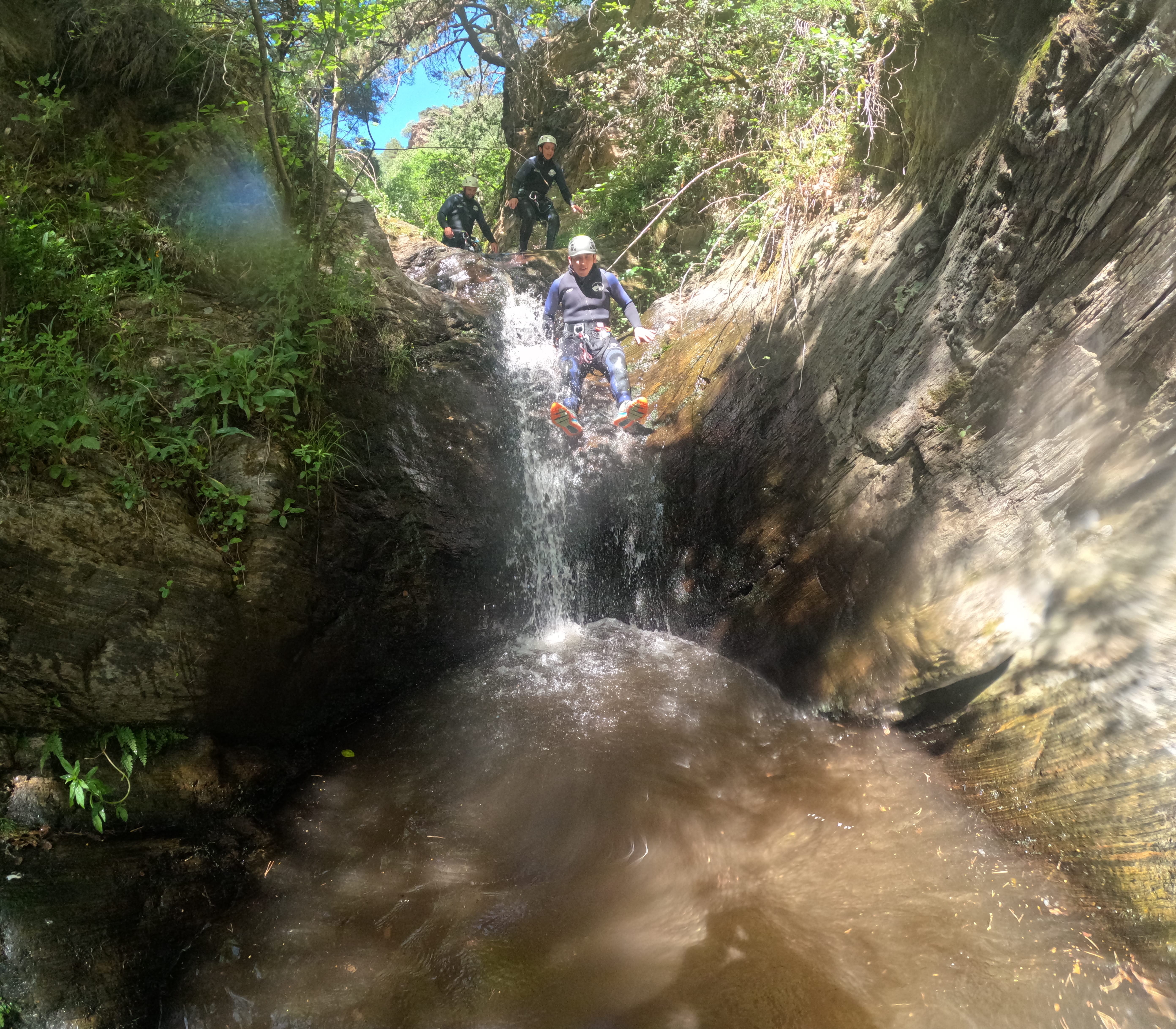 Canyoning participant sliding down a small waterfall into a natural pool in Barranco de Estaron