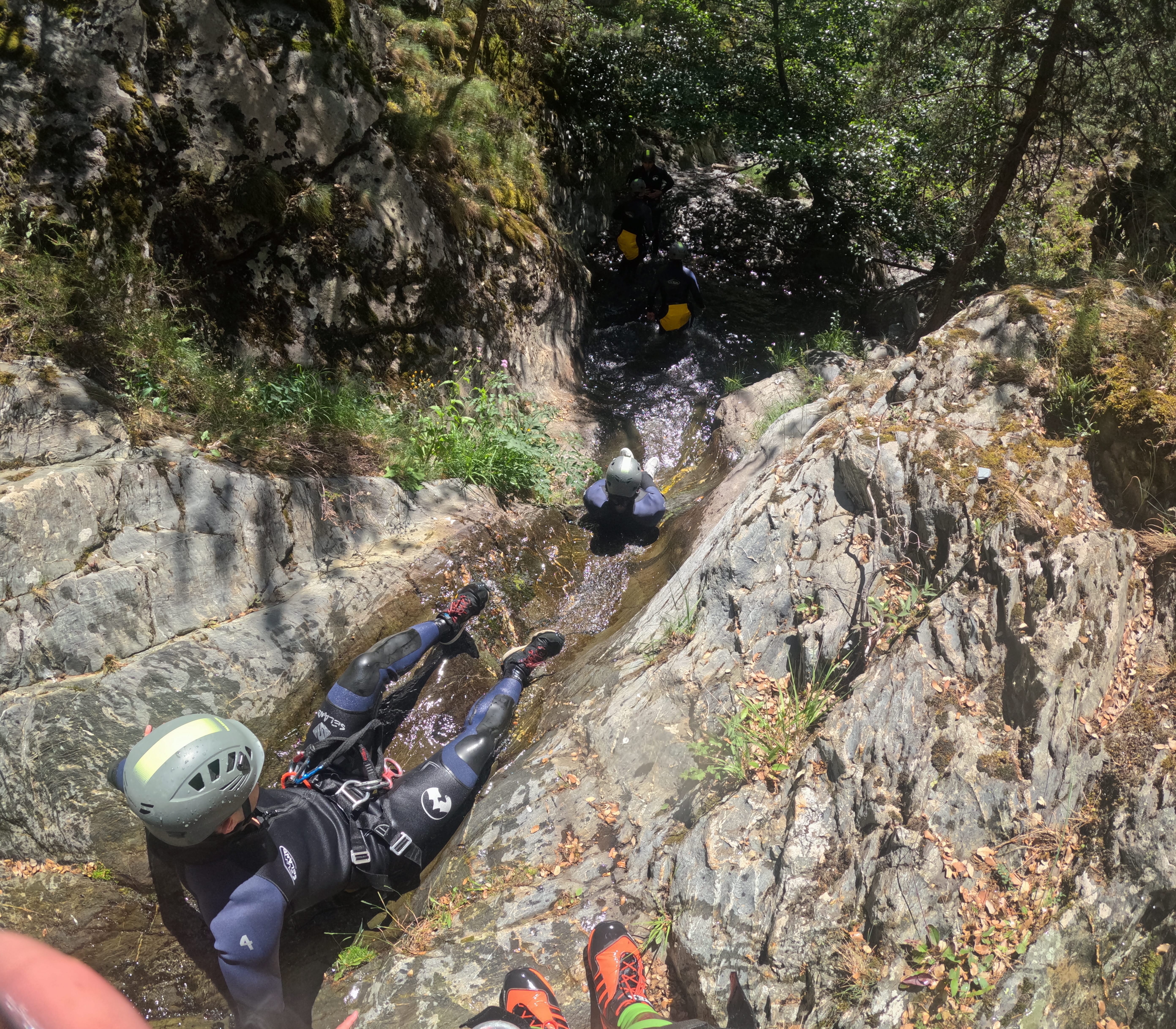 Canyoning participants sliding down a rocky chute into a natural pool in Barranco de Estaron