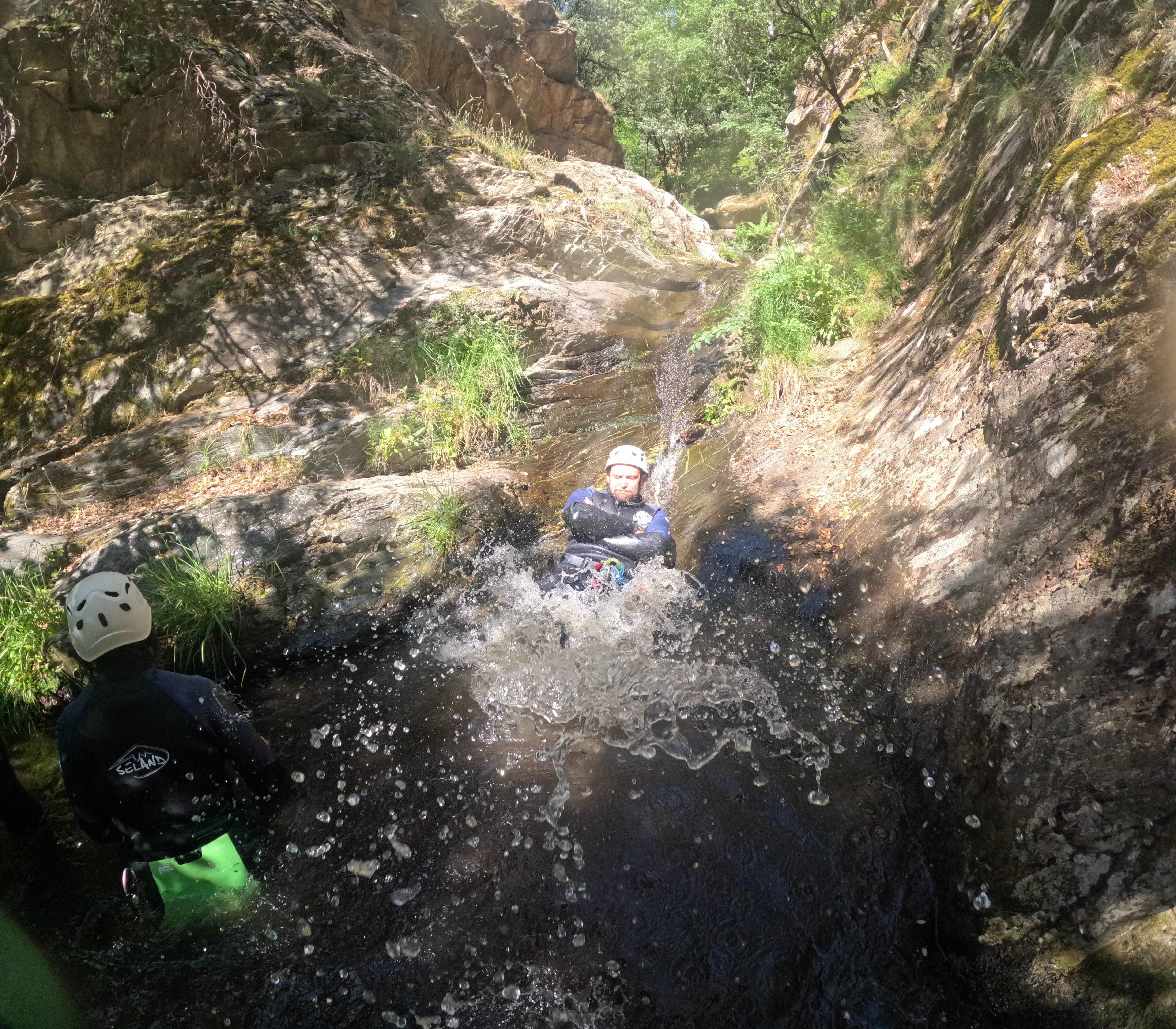 Canyoning participant sliding down a natural rock chute into a pool in Barranco de Estaron
