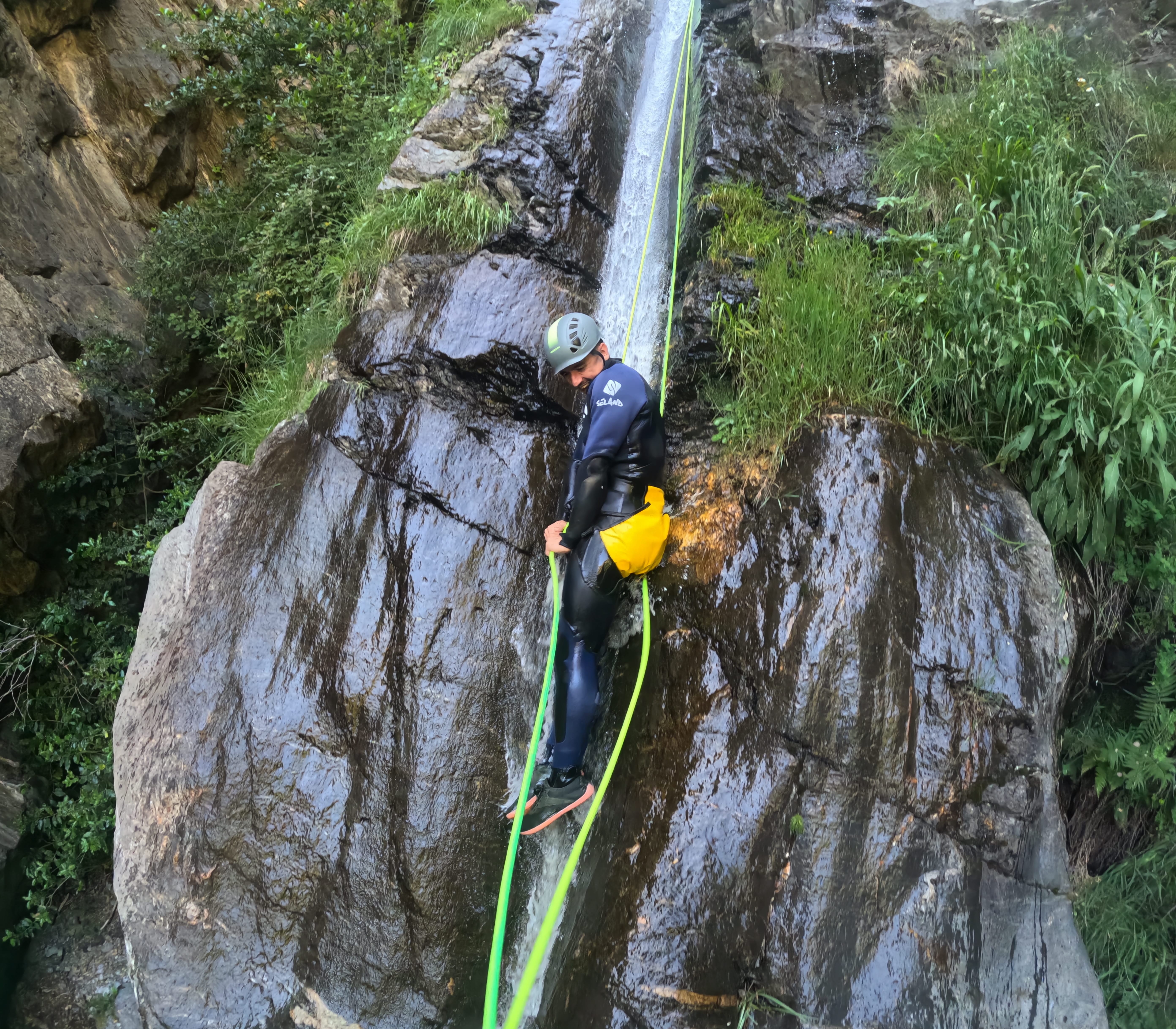 Canyoning participant rappelling down a wet rock face beside a waterfall in Barranco de Estaron