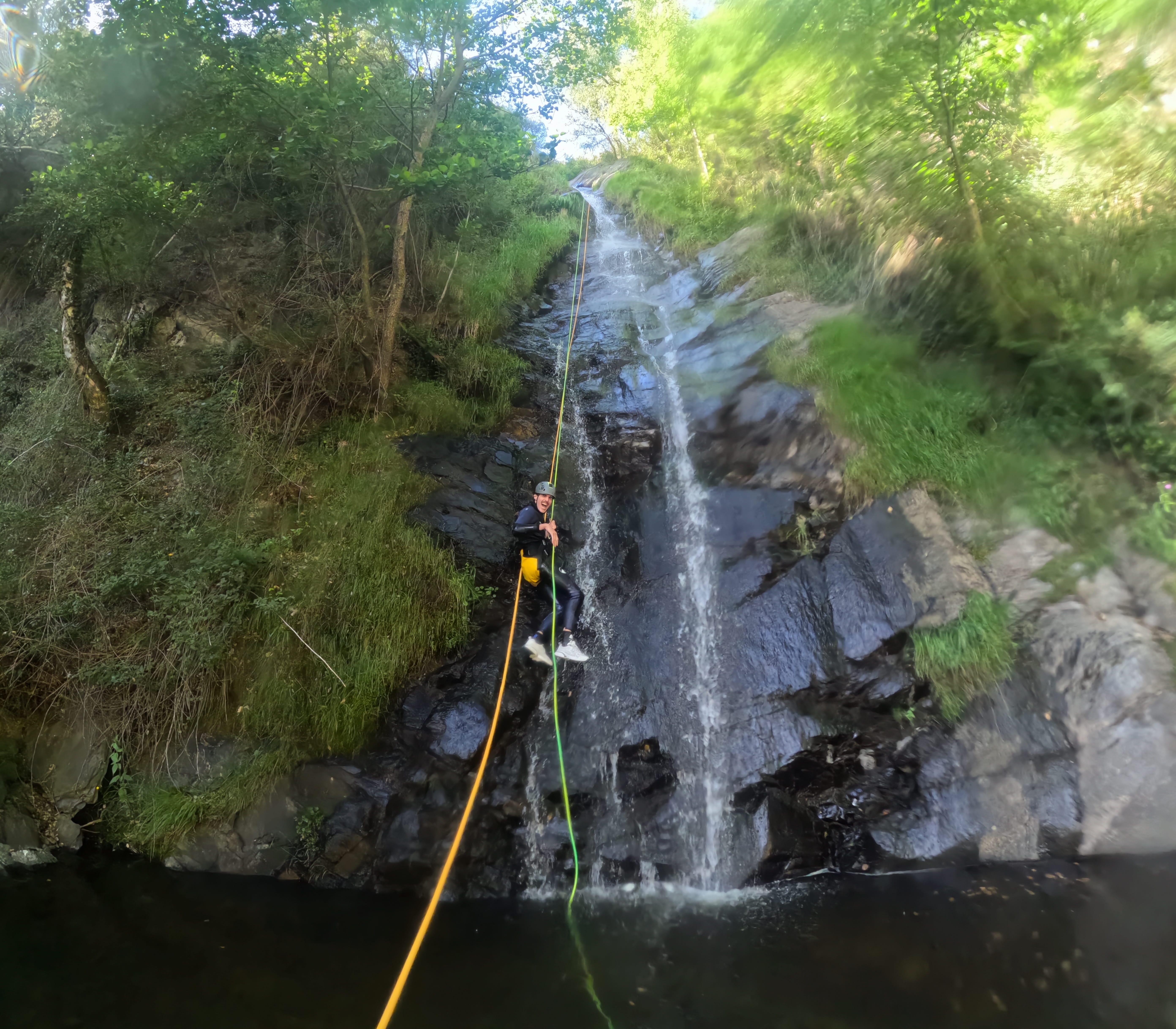 Canyoning participant rappelling down a long waterfall into a natural pool in Barranco de Estaron