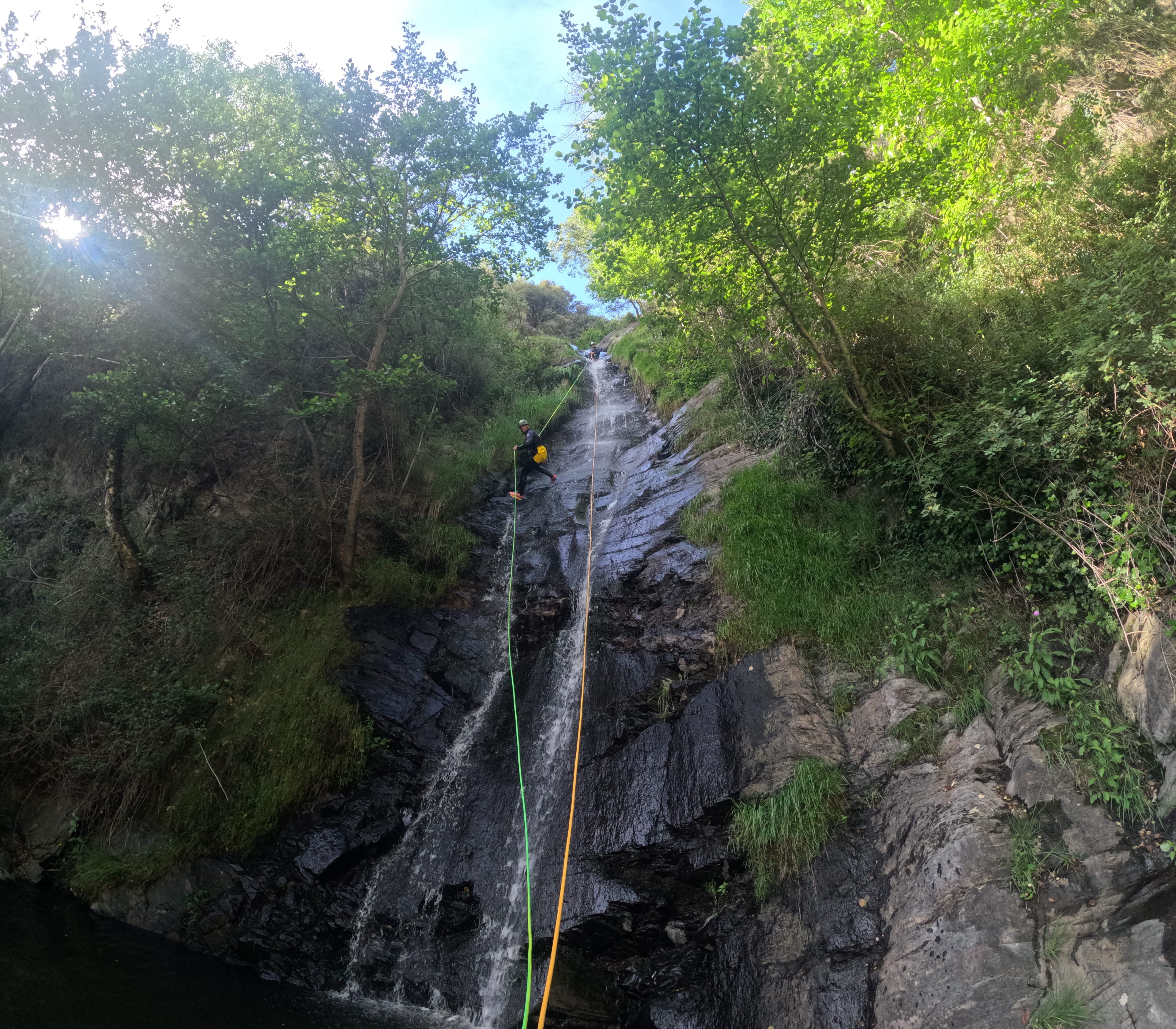 Canyoning participant rappelling down a long waterfall surrounded by lush vegetation in Barranco de Estaron