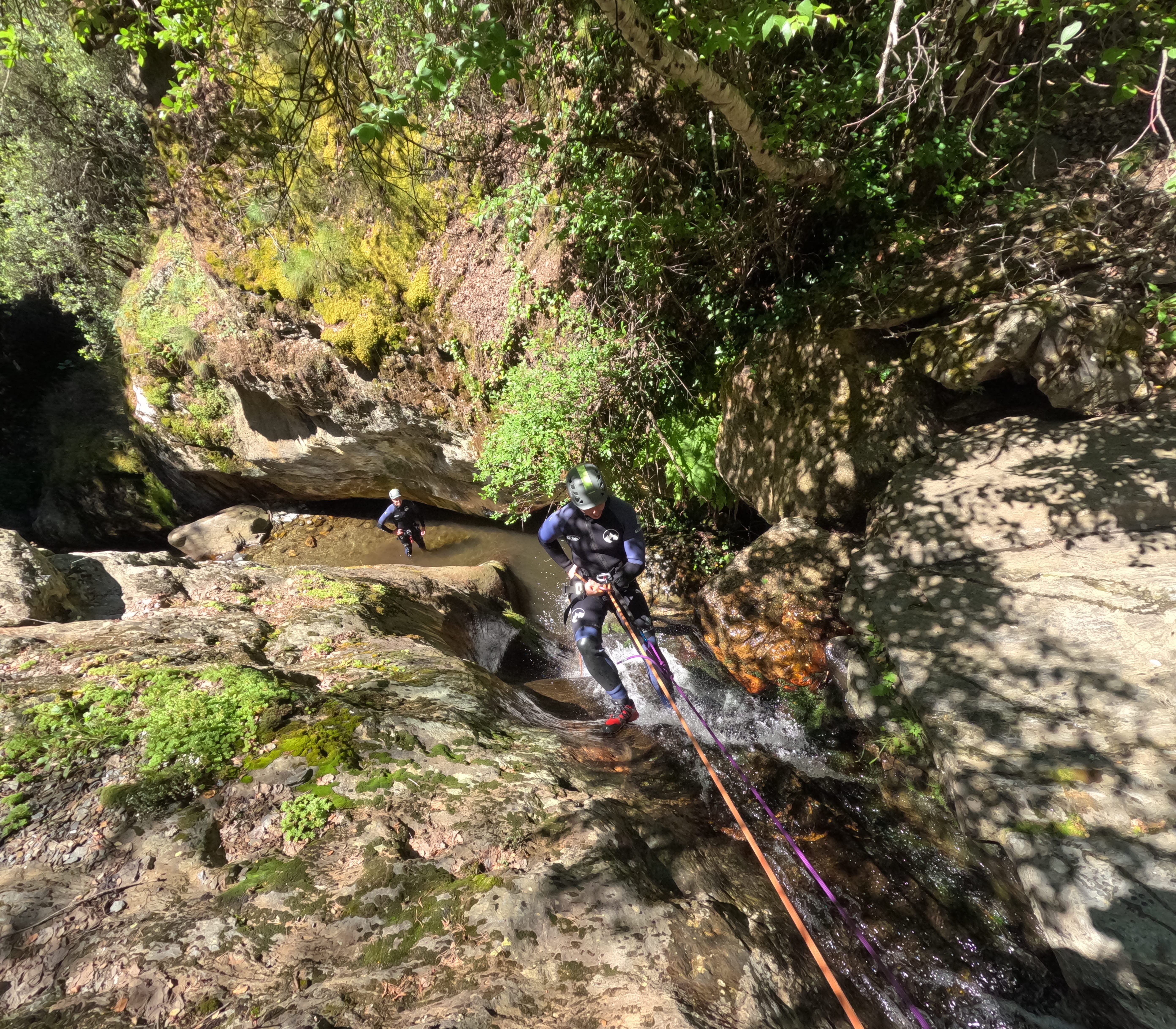 Canyoning participant rappelling down a wet rocky cascade in Barranco de Estaron