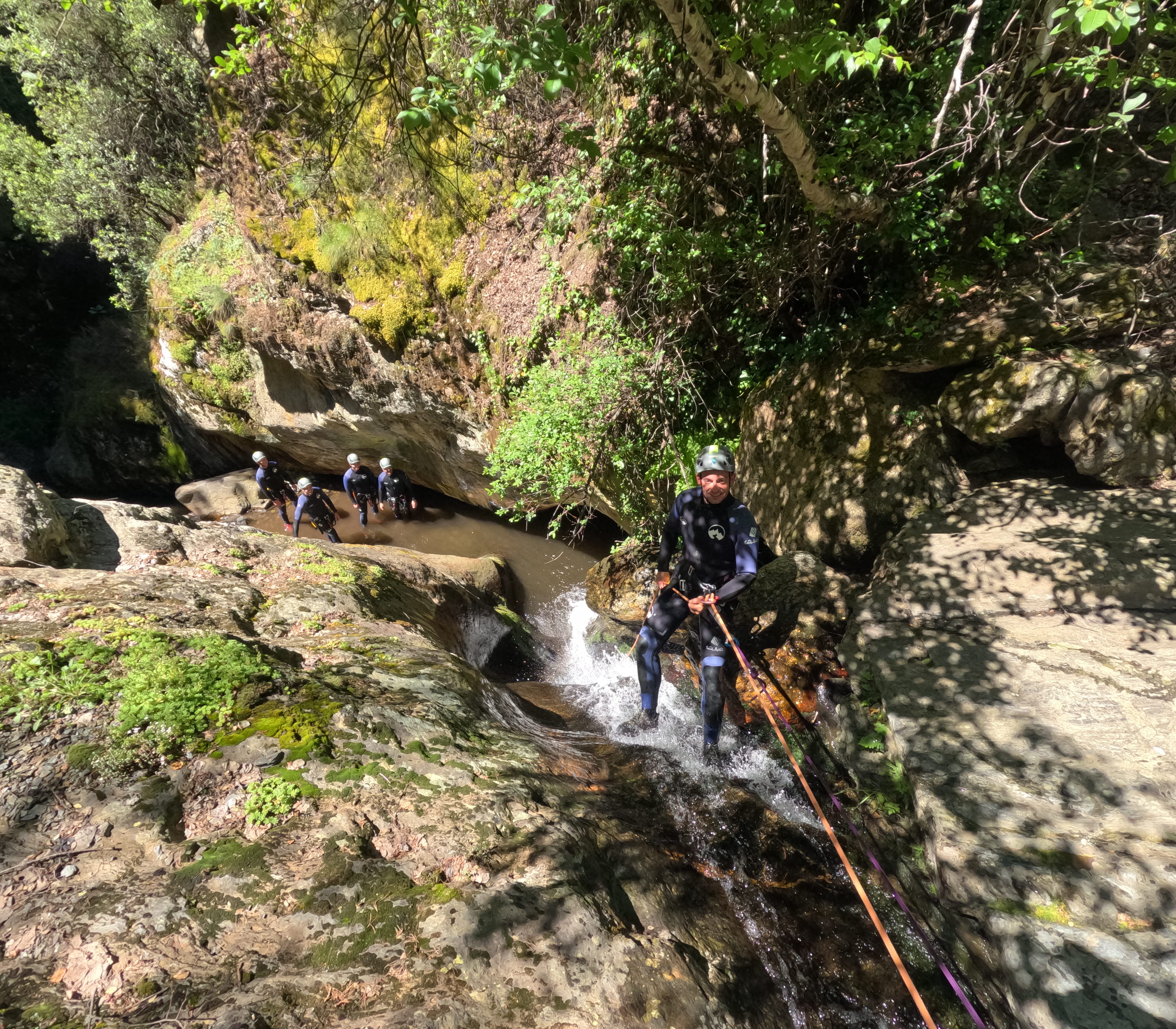 Canyoning participant rappelling down a small waterfall while the group waits below in Barranco de Estaron