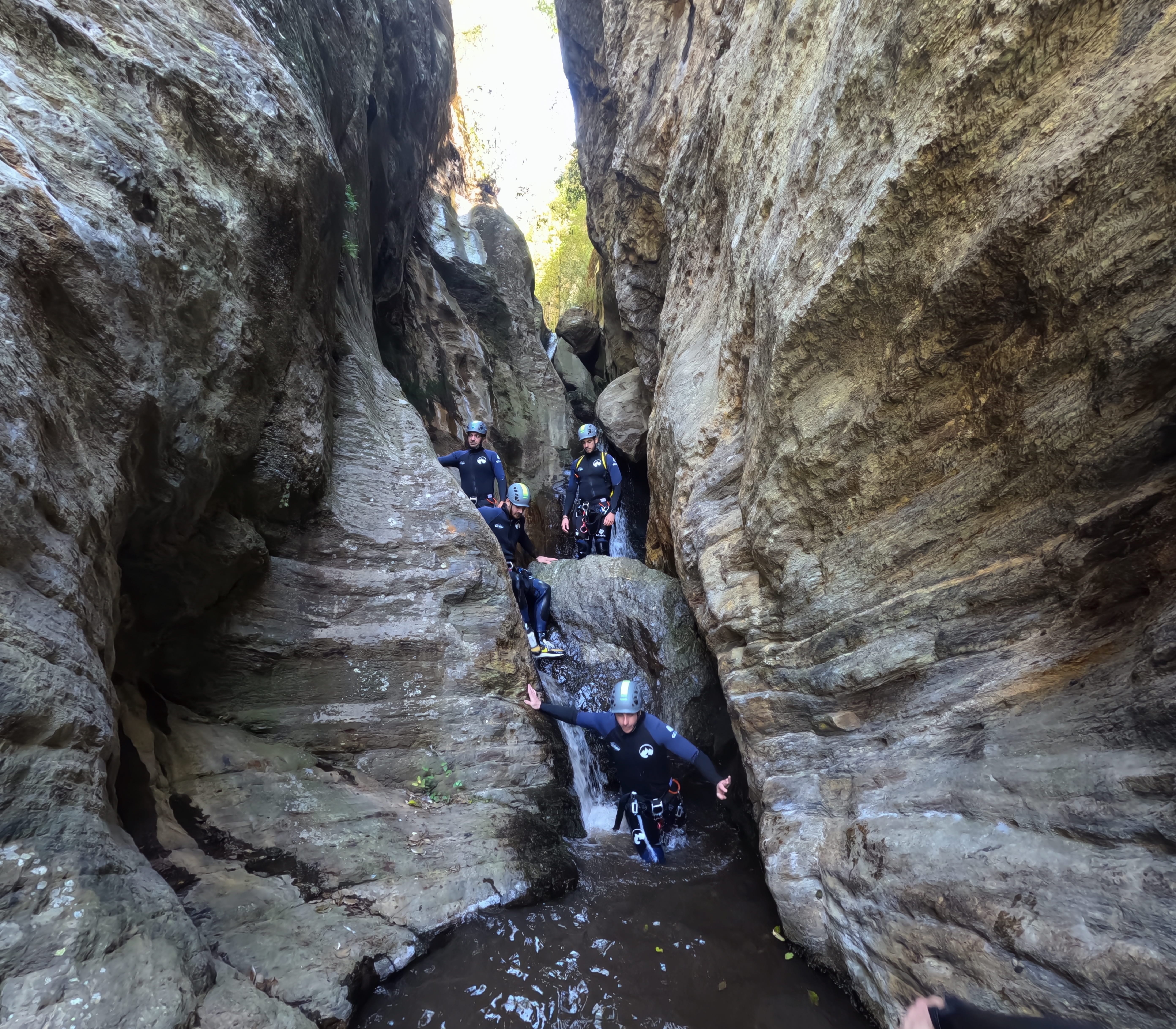 Canyoning group descending through a narrow rocky gorge with water in Barranco de Estaron