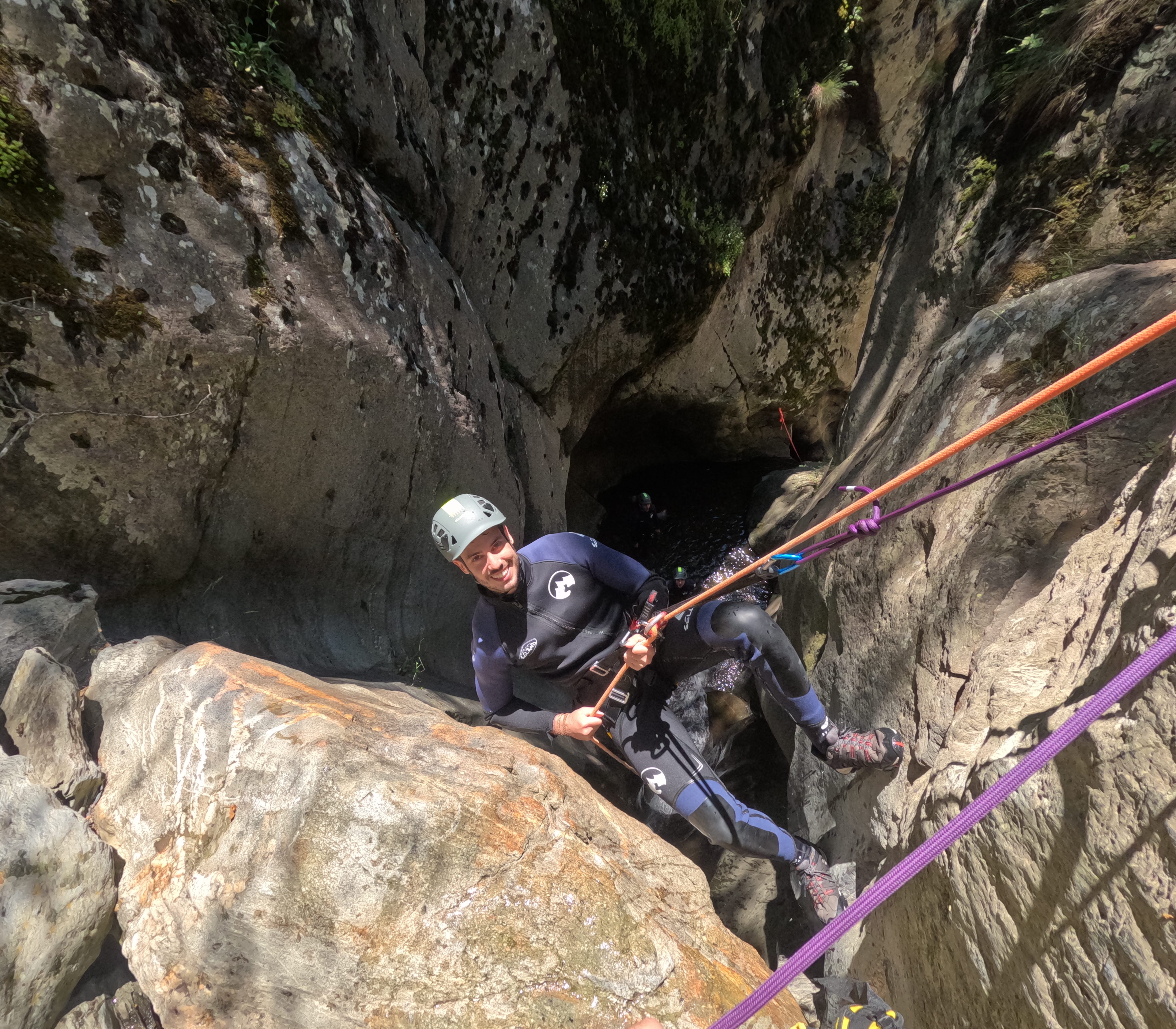 Canyoning participant rappelling beside a large boulder in a narrow section of Barranco de Estaron