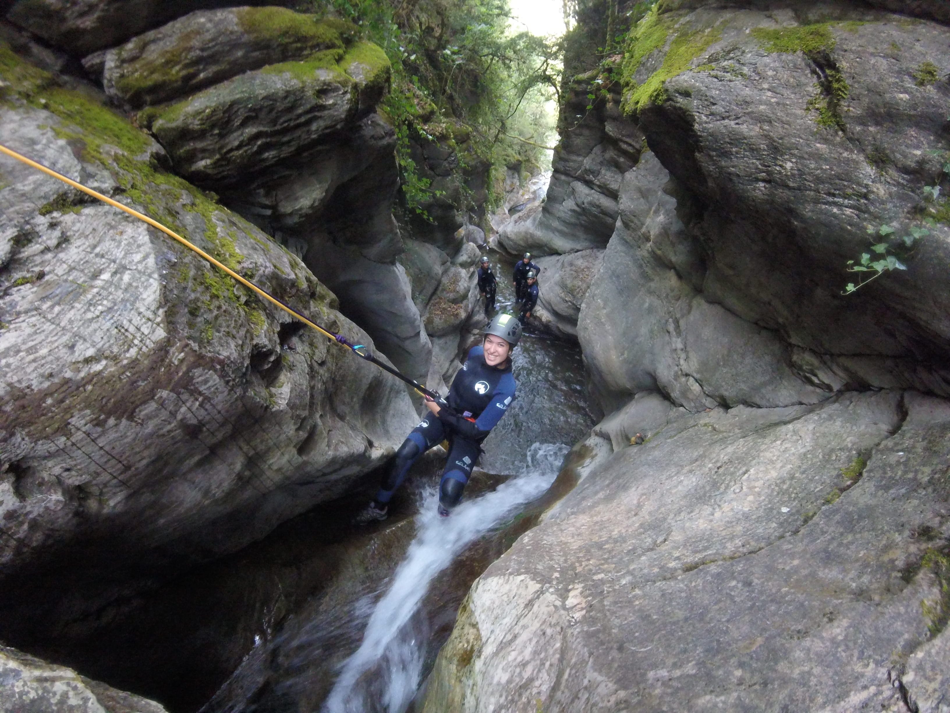 Participant rappelling down a small waterfall through the narrow rocky passage of Les Espones canyon