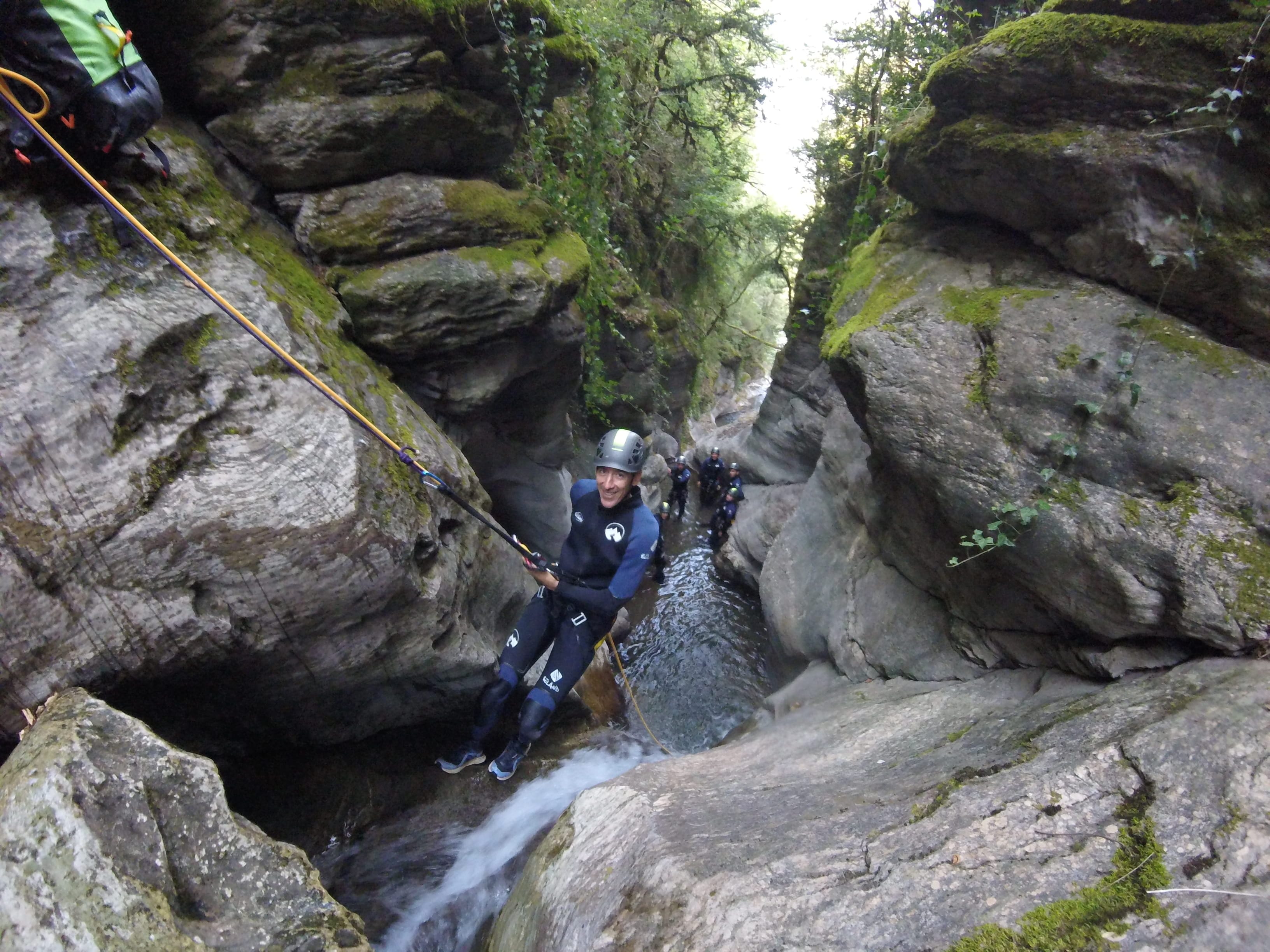 Participant rappelling beside a small waterfall in the narrow, moss-covered gorge of Les Espones canyon
