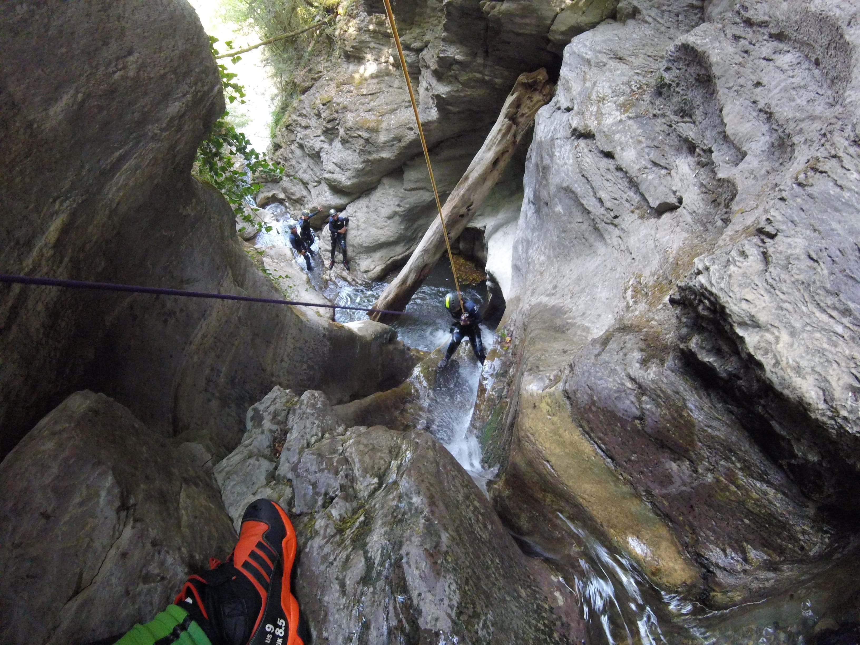 Canyoning participant descending by rope through a narrow waterfall in Les Espones canyon