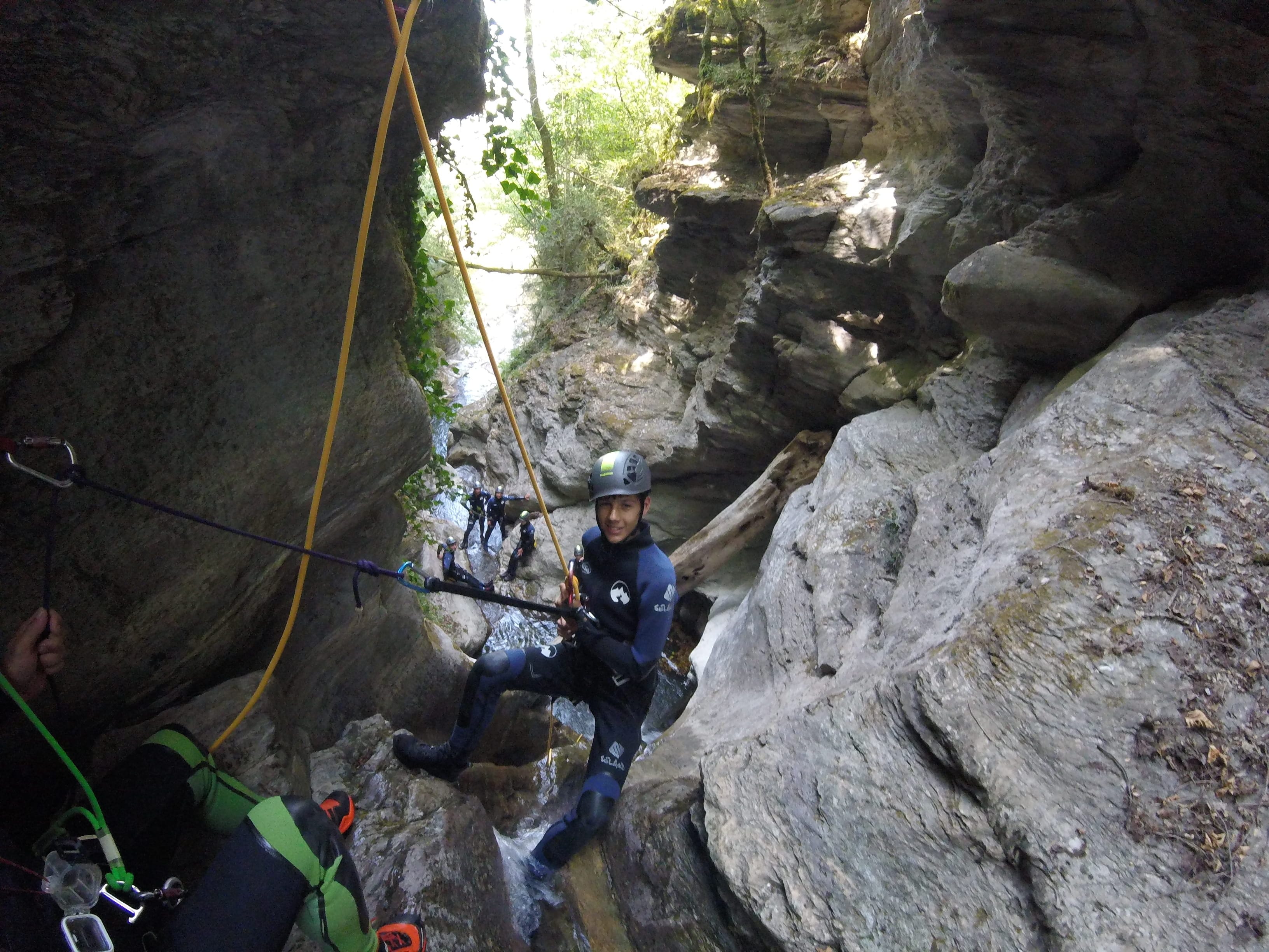 Canyoning participant rappelling through a narrow rocky section of Les Espones canyon