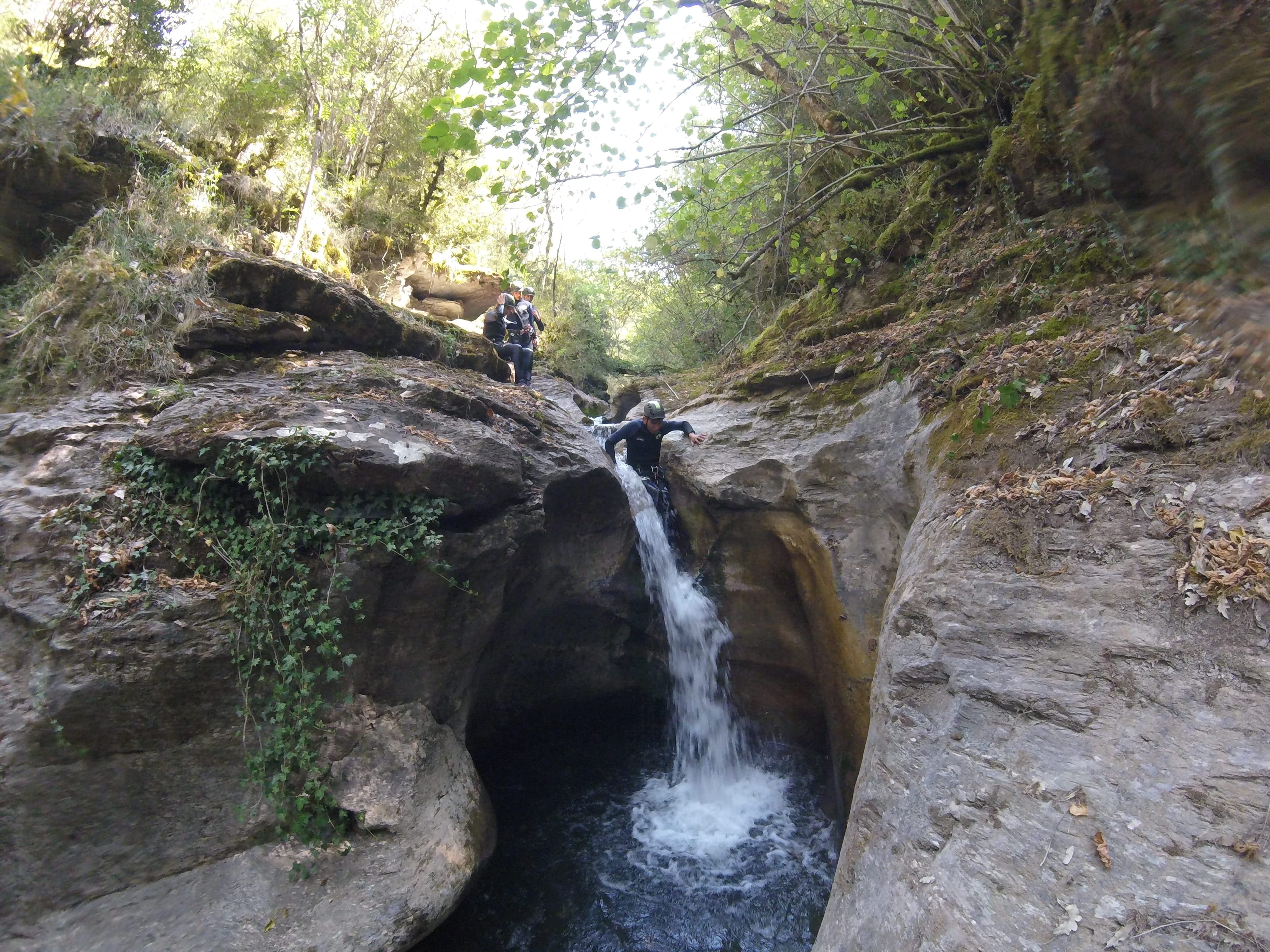 Canyoning participant descending a small waterfall into a natural pool in Les Espones canyon