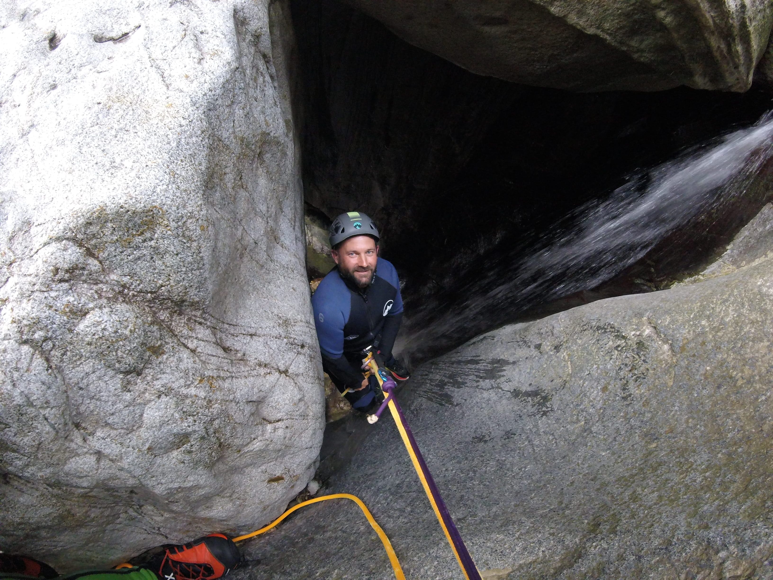 Participant rappelling beside a waterfall through a narrow rocky passage during a canyoning descent in Barranco de Berrós