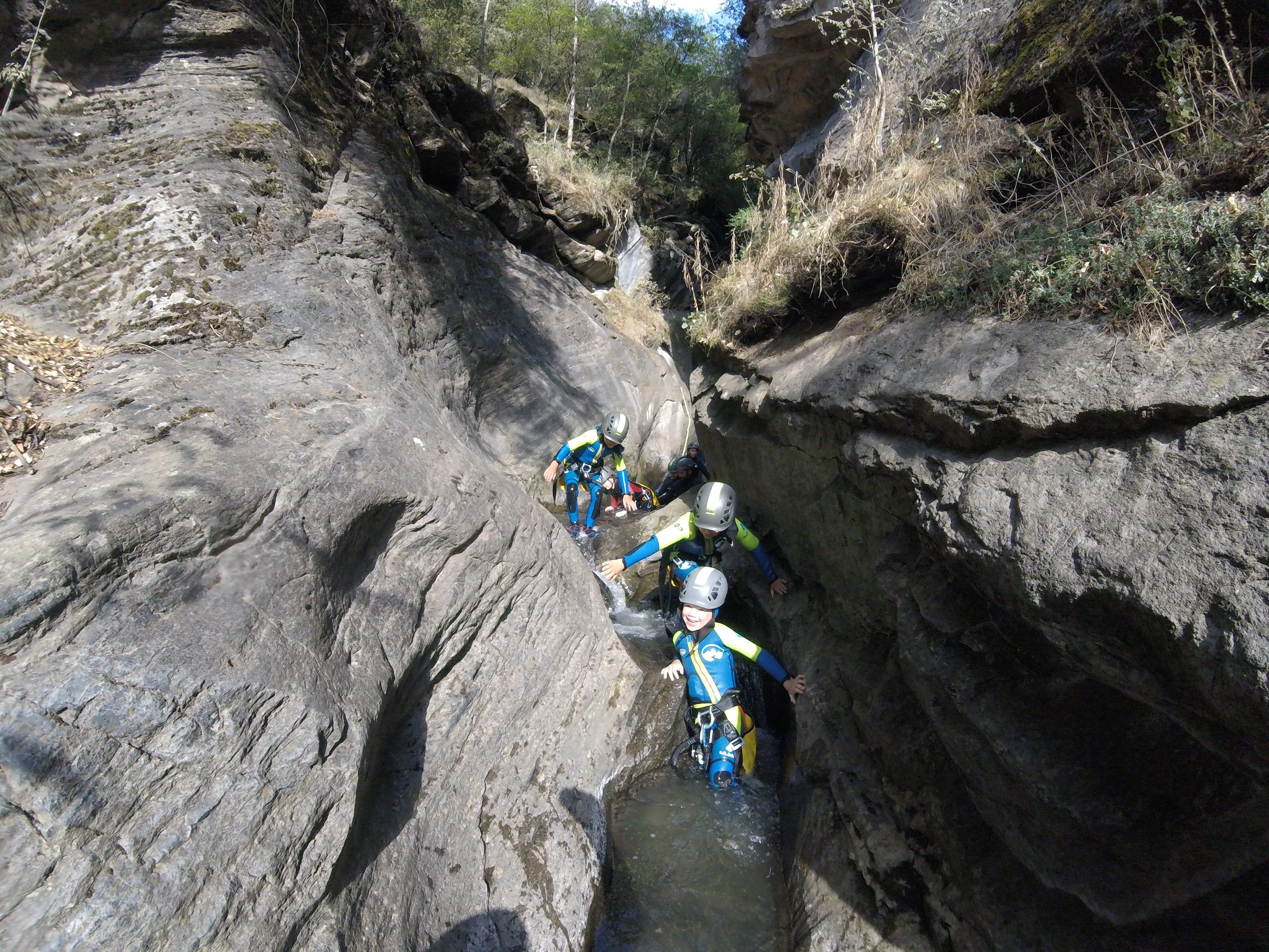 Participants moving through a narrow rocky section with flowing water during a canyoning descent in Barranco de Berrós