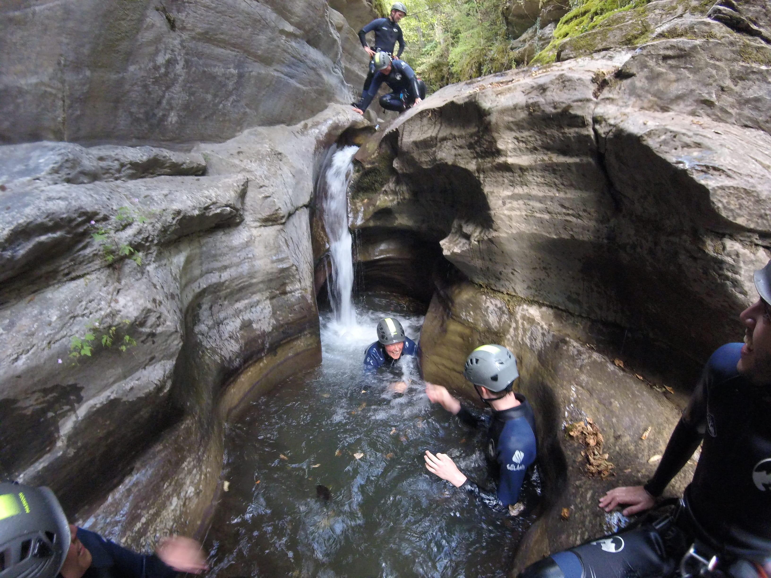 Canyoning group crossing a narrow natural pool beneath a small waterfall in Les Espones canyon
